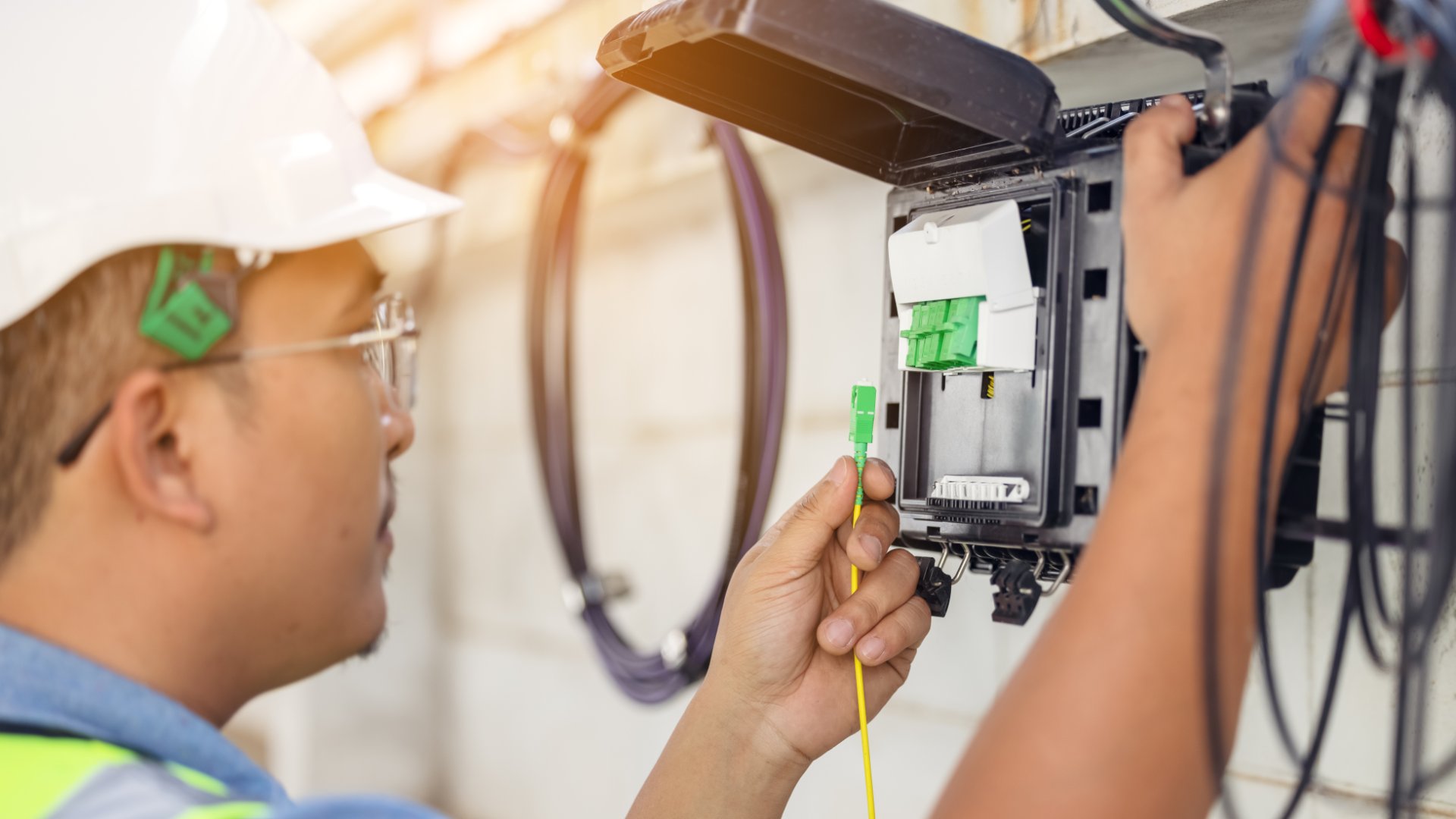 A fiber technician works on an exterior-mounted fiber box. They connect wires and test the connection.