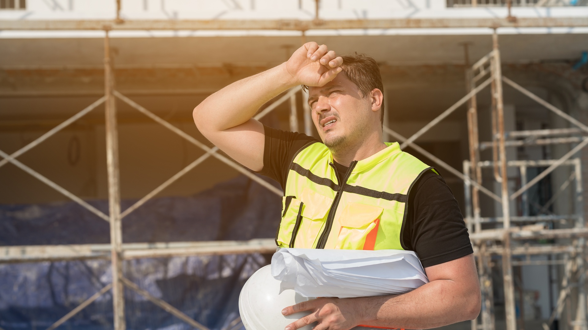 A male construction engineer working, feeling tired and thirsty for water at an outdoor construction site.