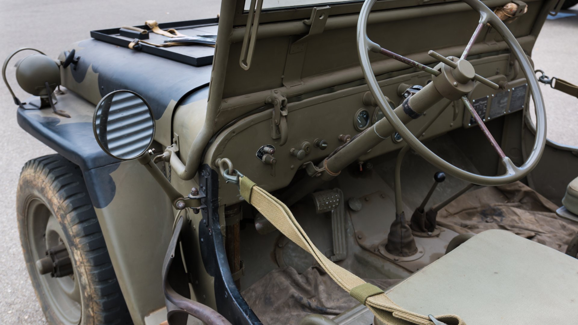 The interior of a dark-green-colored vintage World War II era Willy's jeep. The steering wheel and seats are shown.