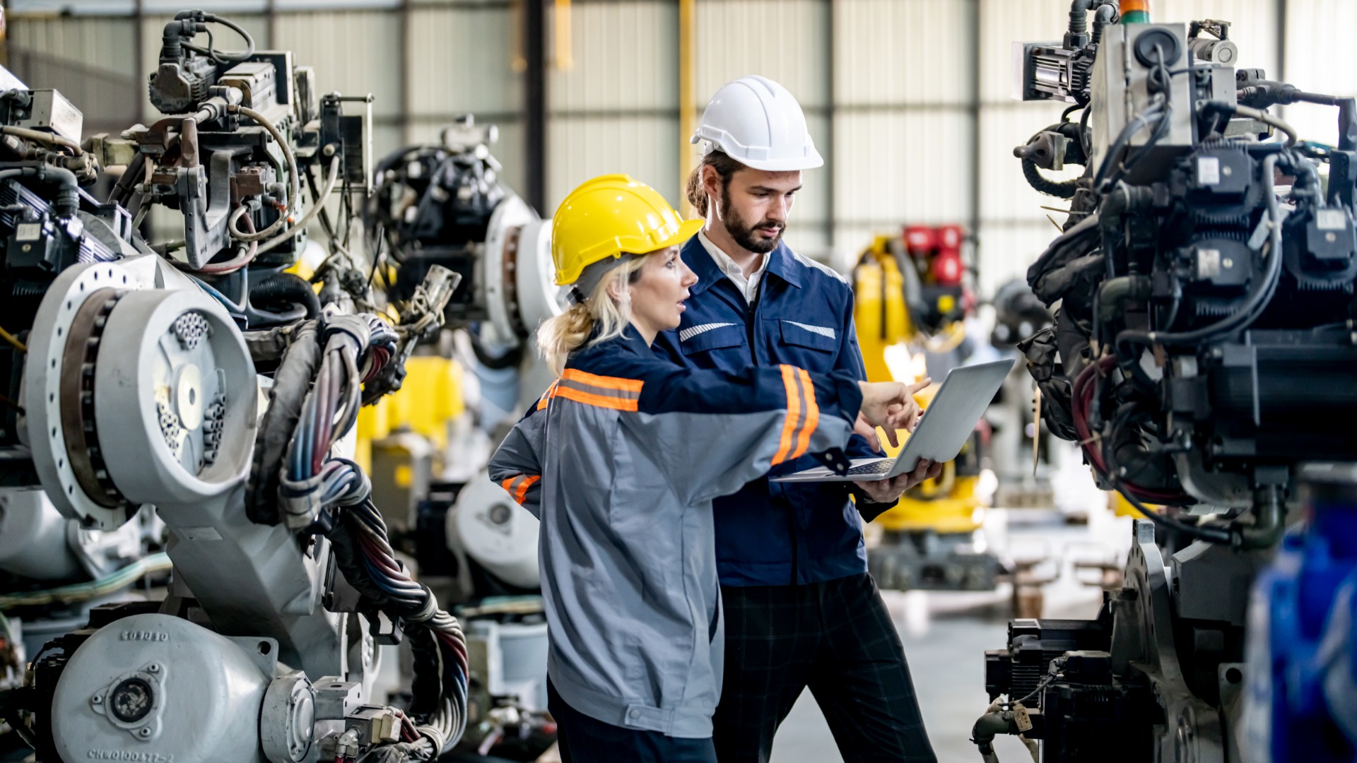 A woman is standing next to a man; both are wearing hard hats and are standing in an industrial facility.