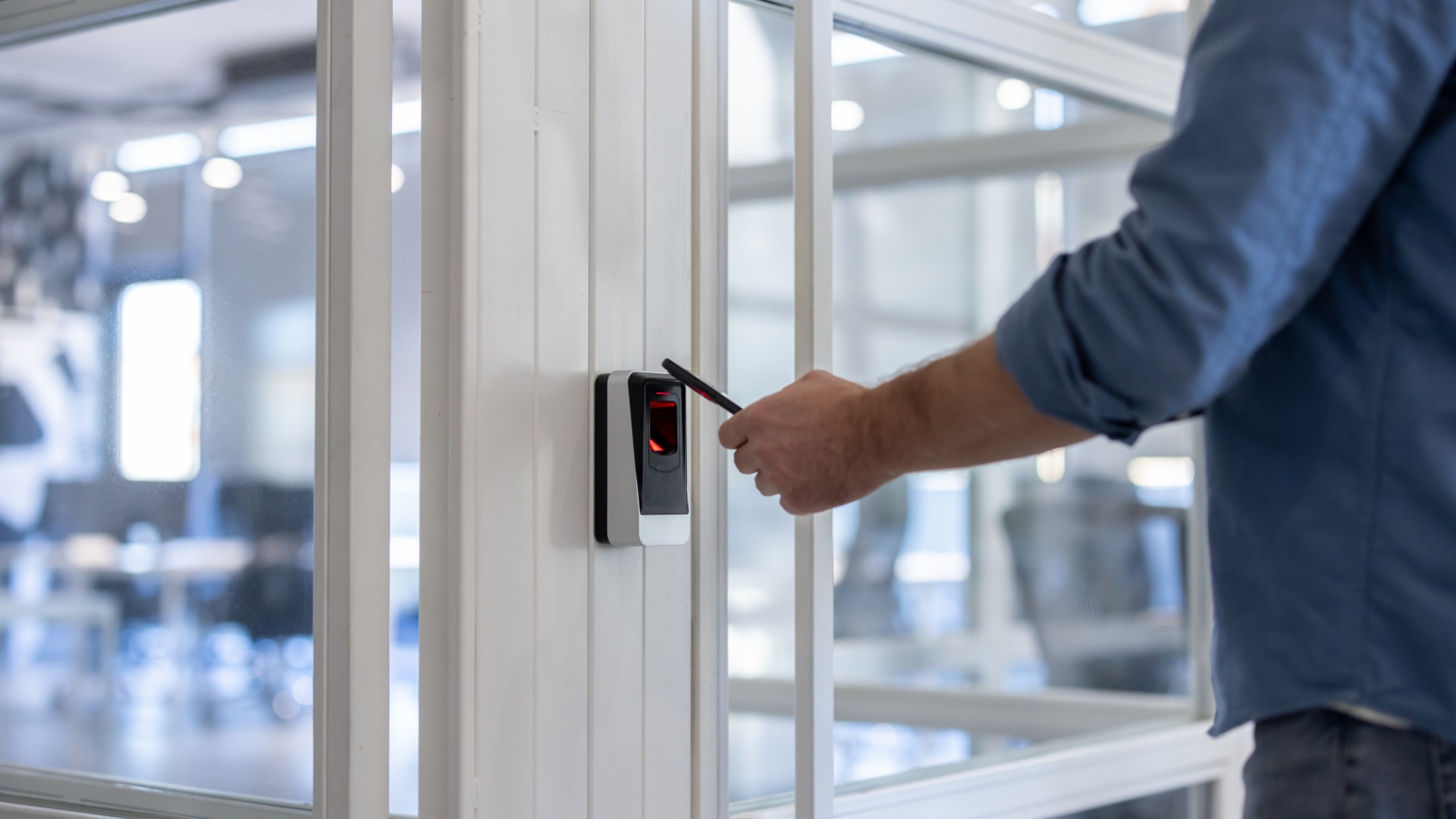 A close-up of a man holding out a key card to a wall-mounted scanner to open a white door in an office.