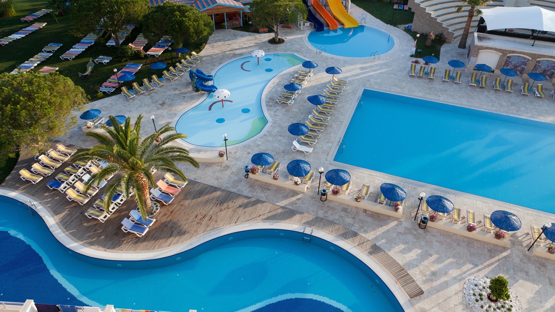 An overhead view of a swimming pool area at a luxury hotel. There are waterslides and a shallow play area for kids.