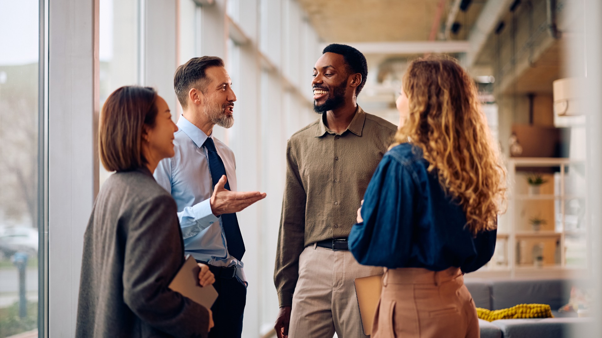 A group of people dressed in business casual attire are standing around in an interior space chatting.