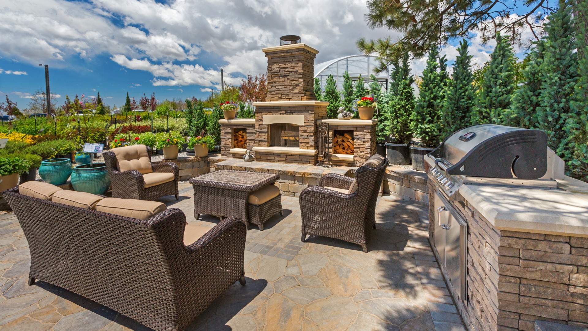 A backyard patio with a fireplace and a stone off to the side. The sun is out and there are green trees in the background.