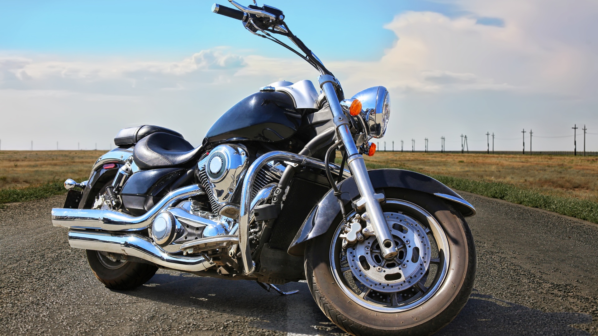 A black and silver motorcycle parked in the middle of a highway road lined by open fields on both sides.