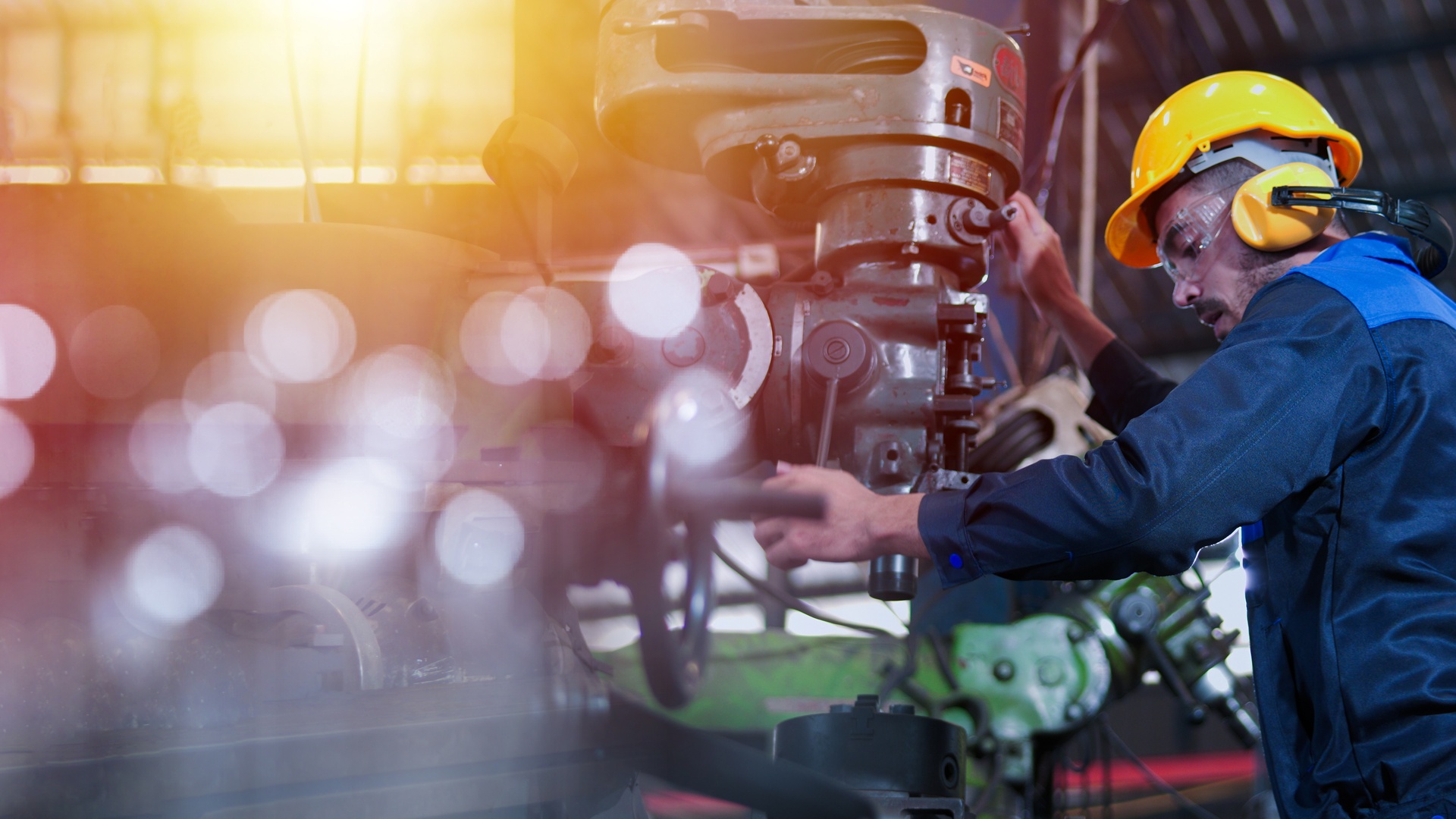 A factory worker operating a piece of machinery while wearing a hard hat, safety glasses, and ear protection.