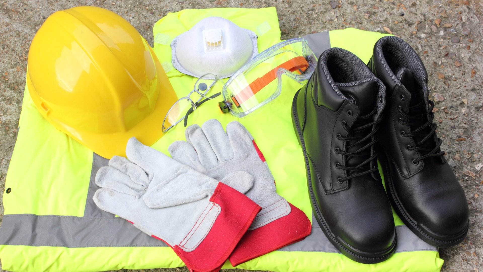 Several pieces of personal protection equipment lie on a concrete surface, including a helmet and gloves.