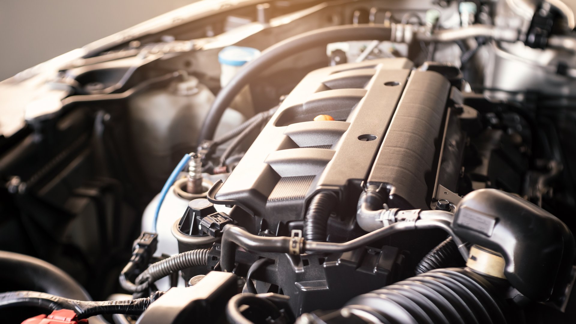 A close-up of a modern car engine in a warehouse setting with the sun peaking through and highlighting the components.