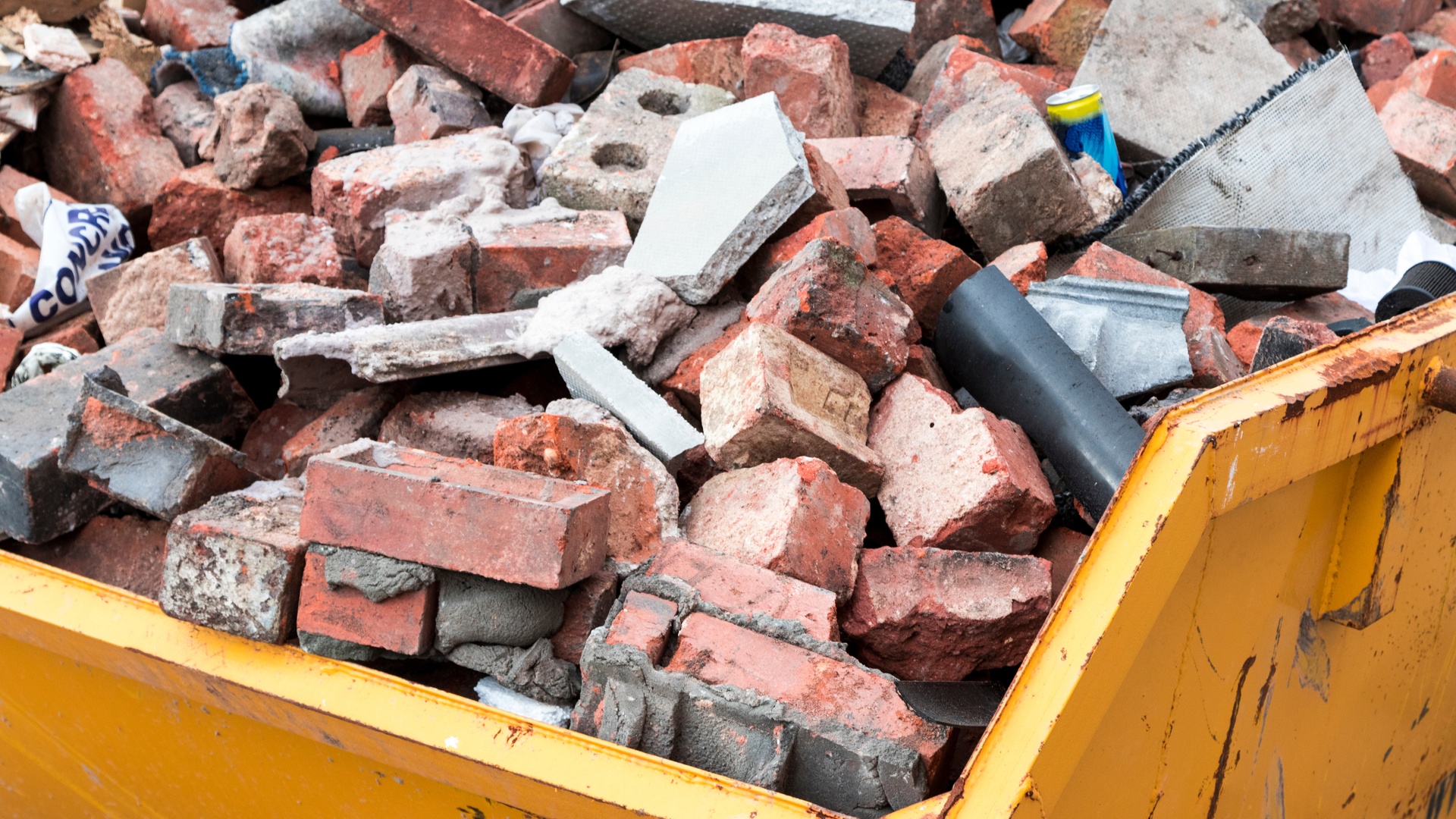 A yellow dumpster full of bricks and other construction waste materials.