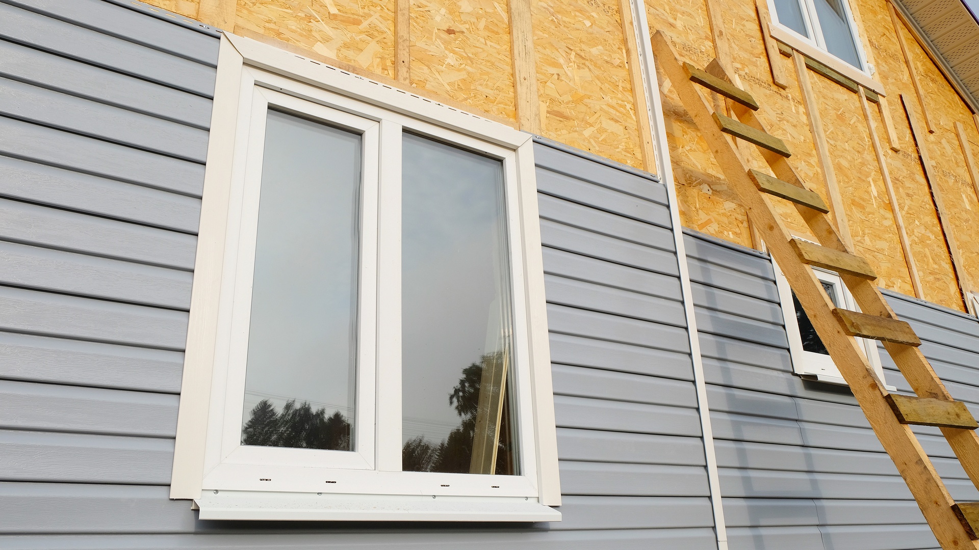 The exterior of a home with a ladder leaning against it while siding is being put up over wooden slats.