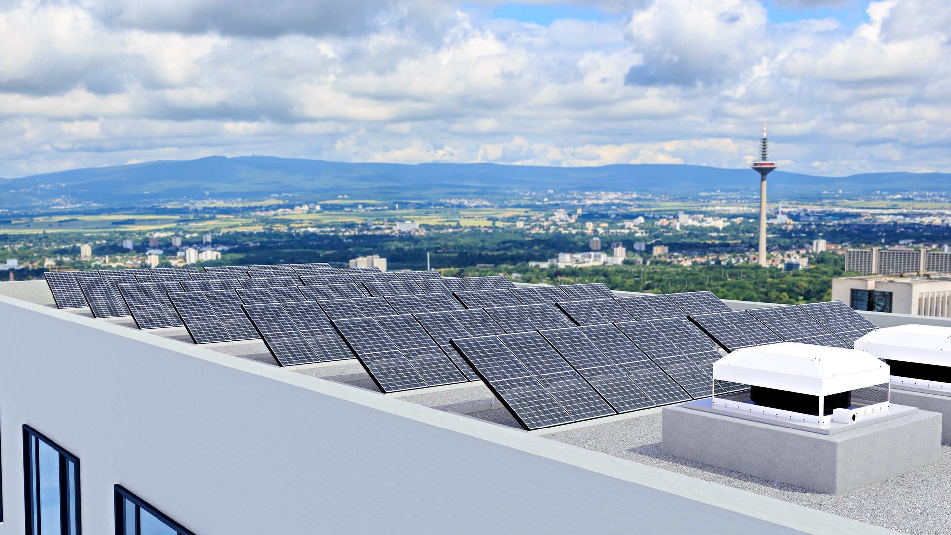 A commercial building with solar panels installed on the roof. Behind the building are other buildings and hills.