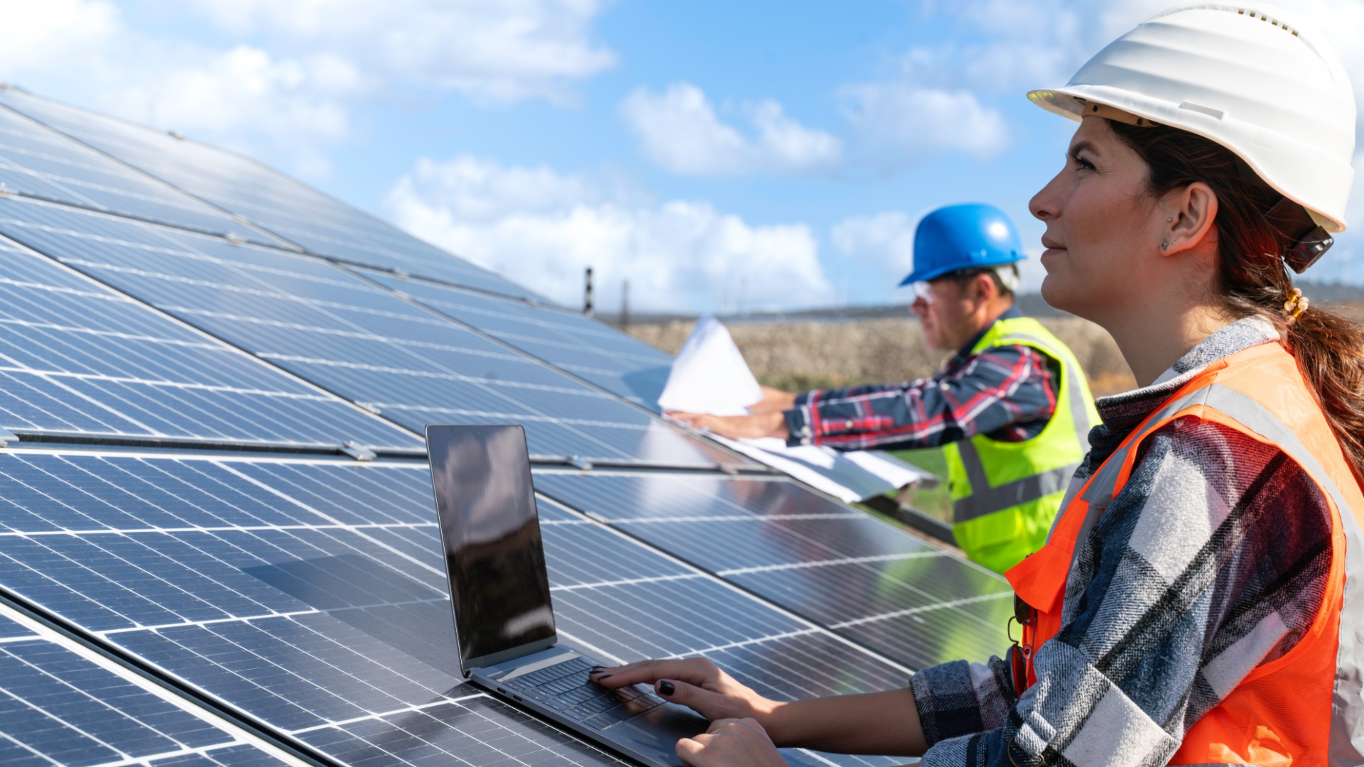 A young engineer is inspecting a solar panel installation. She has a laptop placed on a set of panels.