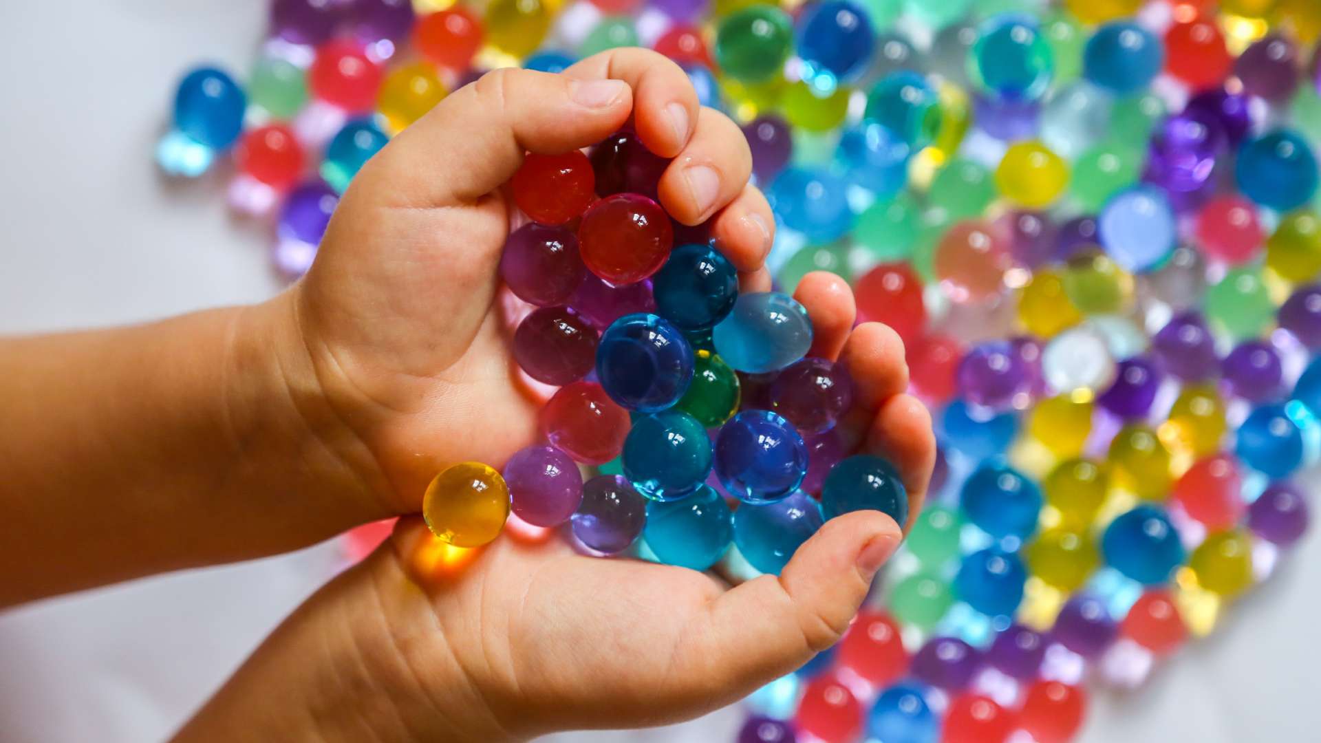 A child’s hands holding a variety of brightly colored hydrogel balls, showcasing their texture and translucence.