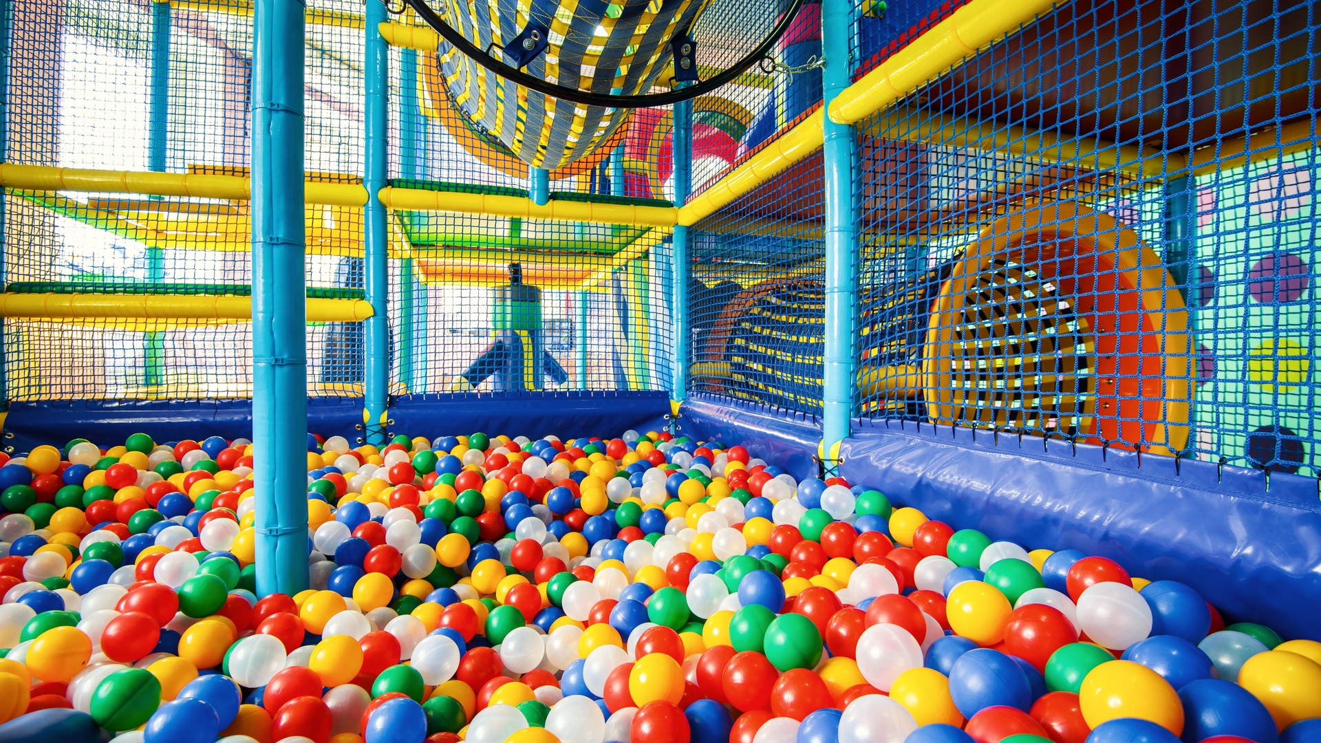 A colorful ball pit surrounded by netting and tunnels in an indoor playground.