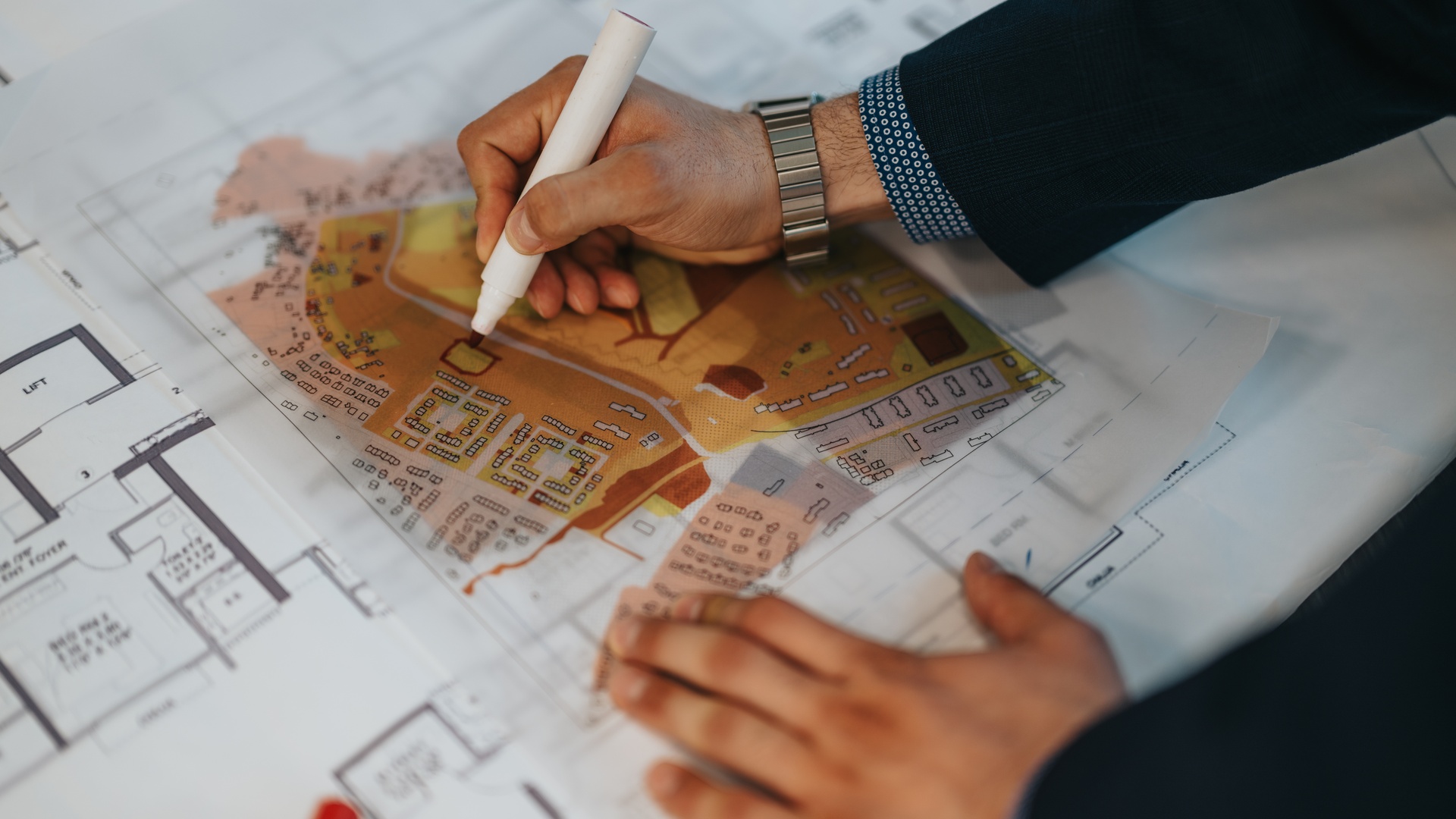 A person using a red dry-erase marker to work on a transparent overlay of an architectural drawing of a community.