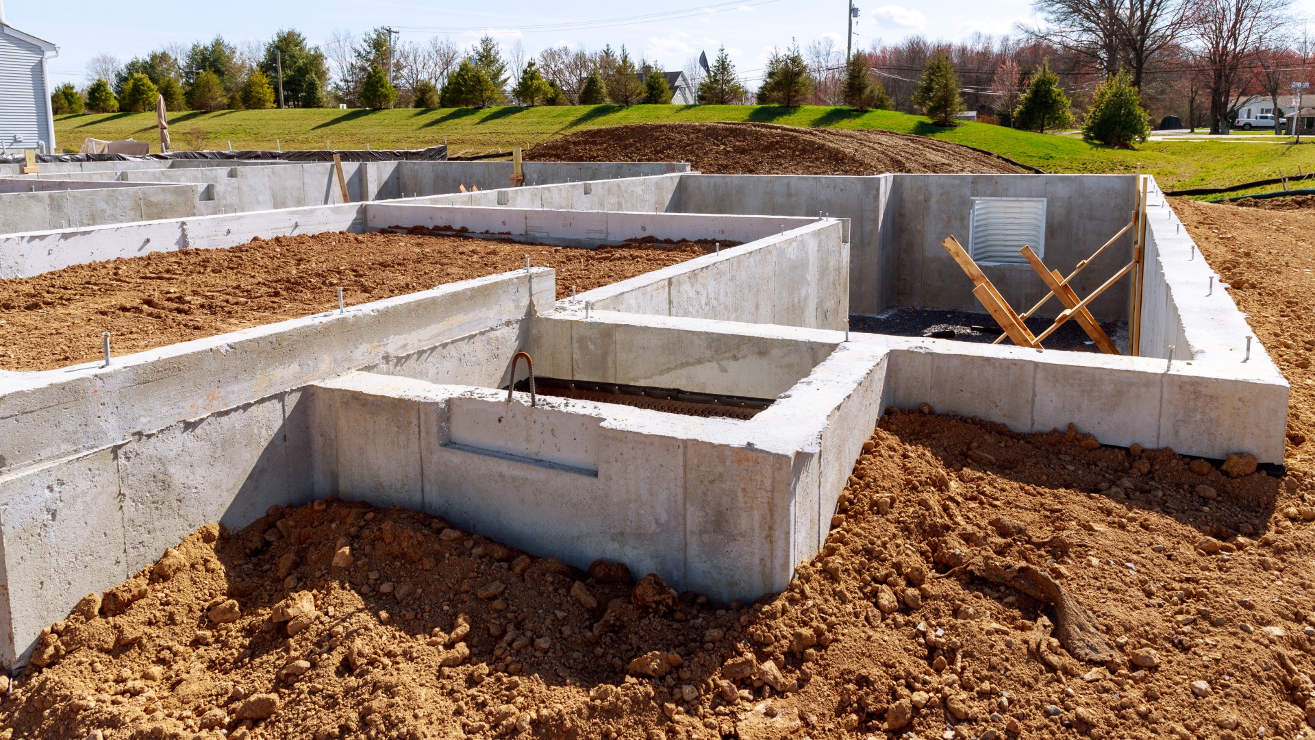 Concrete foundation with metal reinforcement at a house construction site, showing an early stage of the build.