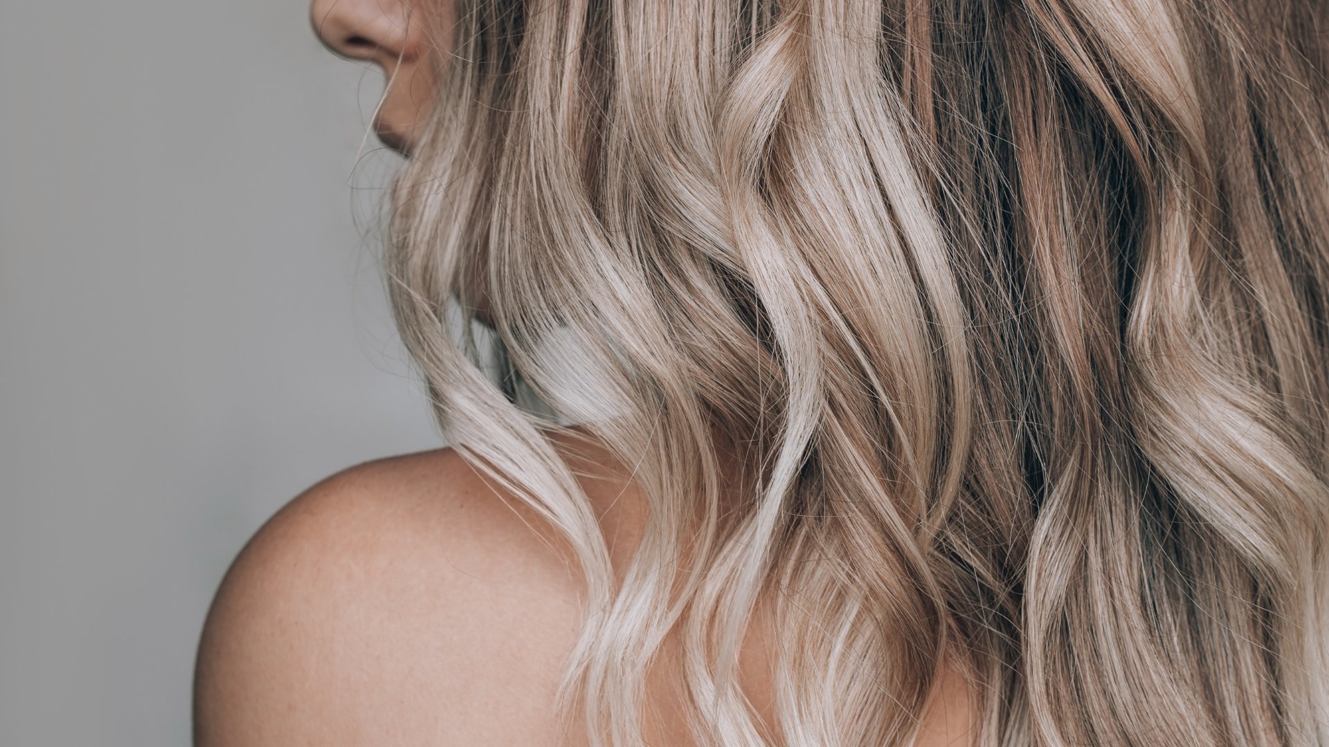 Close-up of a woman turning her head to the side. Her long, wavy blonde hair falls gently over her bare shoulder.