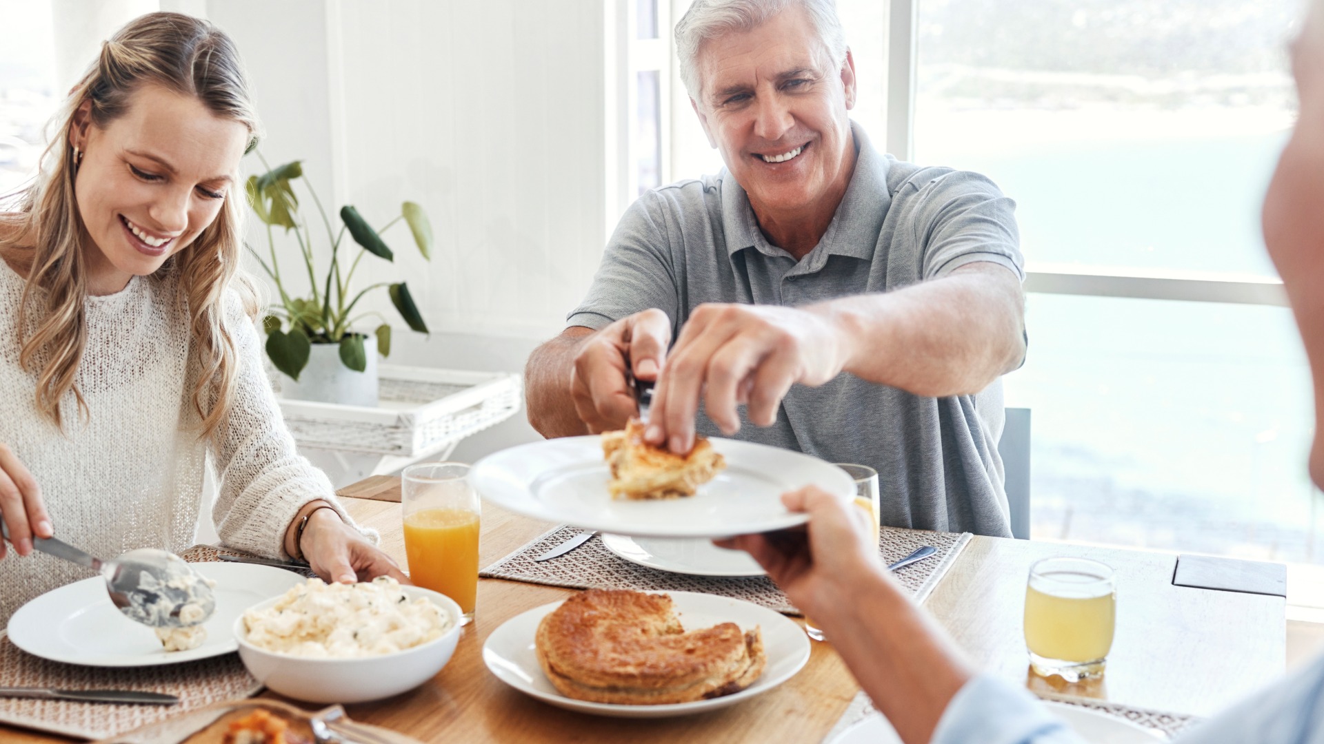 Smiling family enjoying a meal together at a dining table, serving food and sharing a warm, relaxed moment at home.