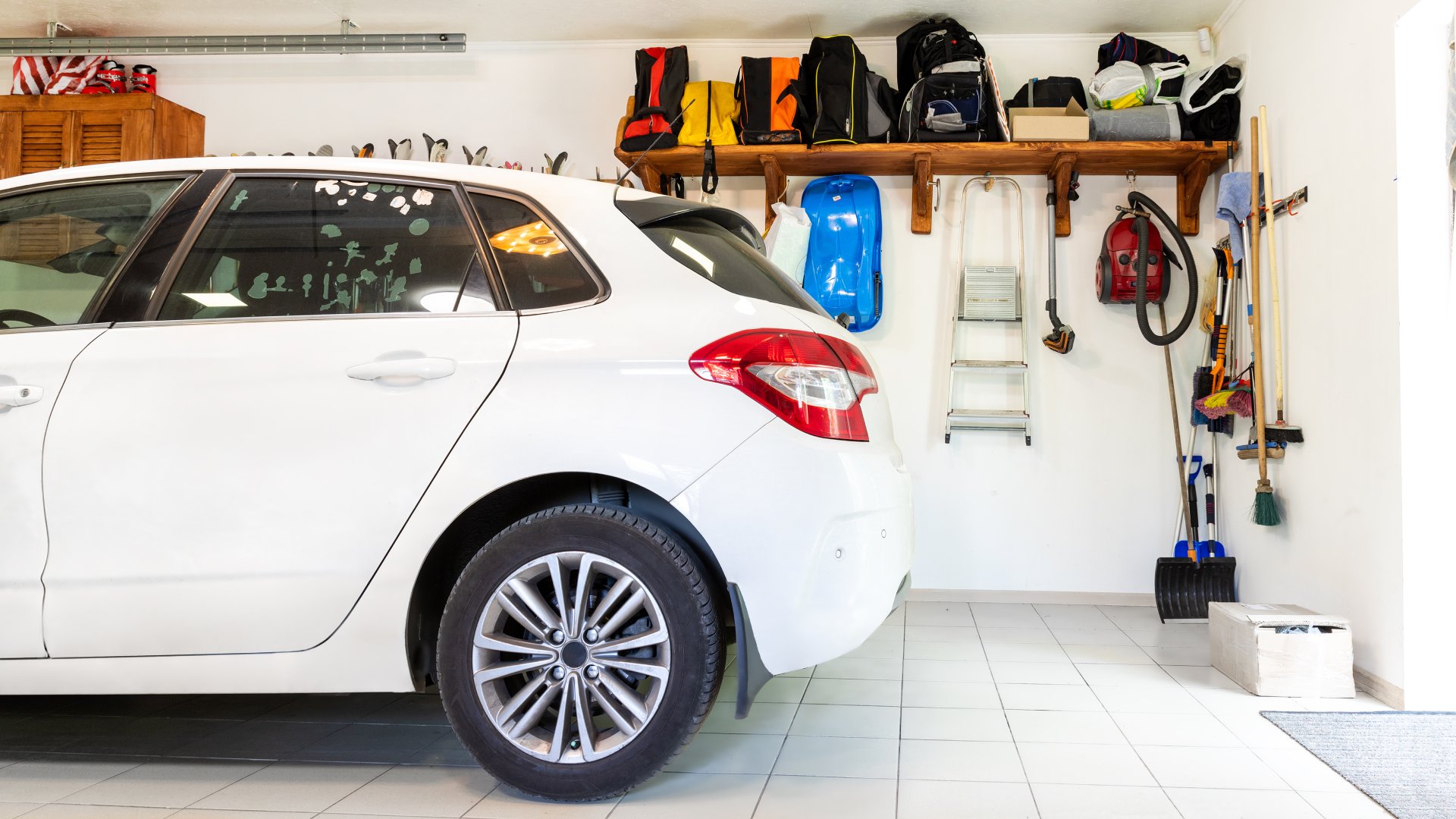 Garage interior with a wooden shelf, tools, and equipment along a white wall with a vehicle parked in the middle.