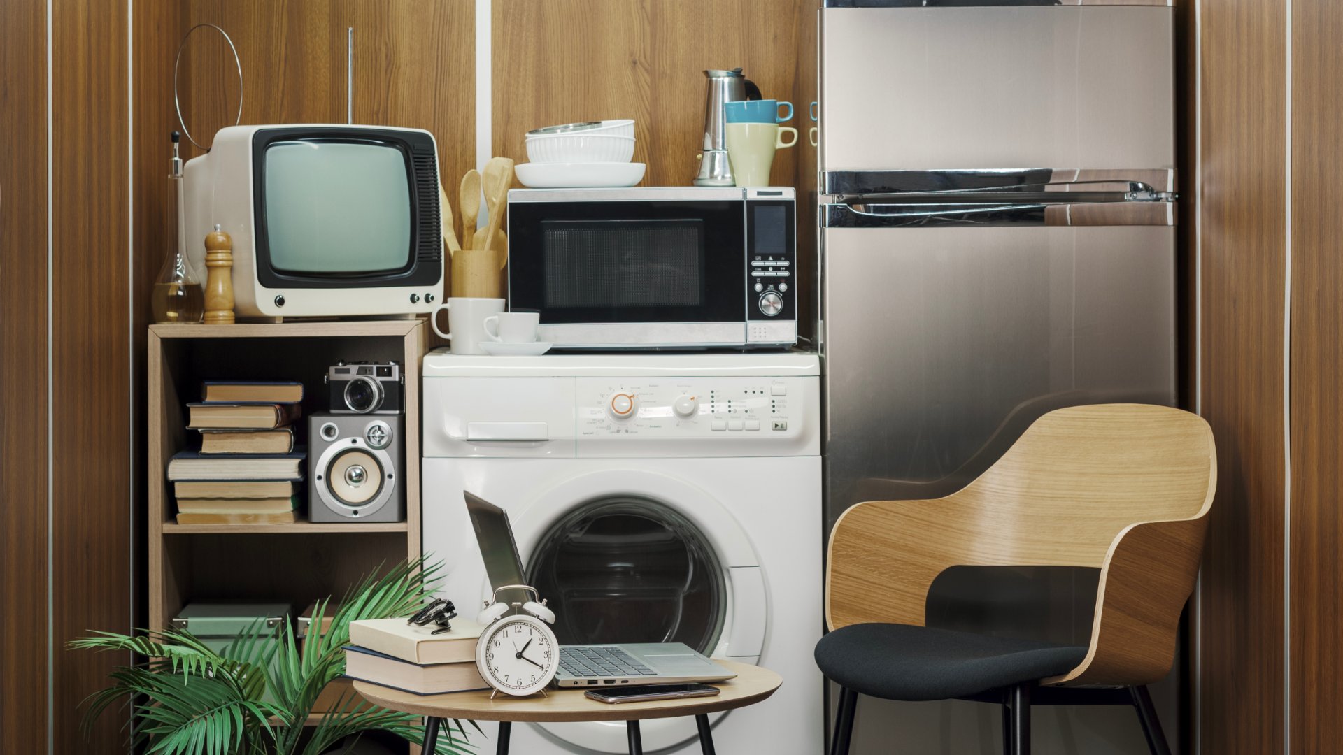 A TV, refrigerator, table, and laundry machine are squeezed together in a small, confining space.