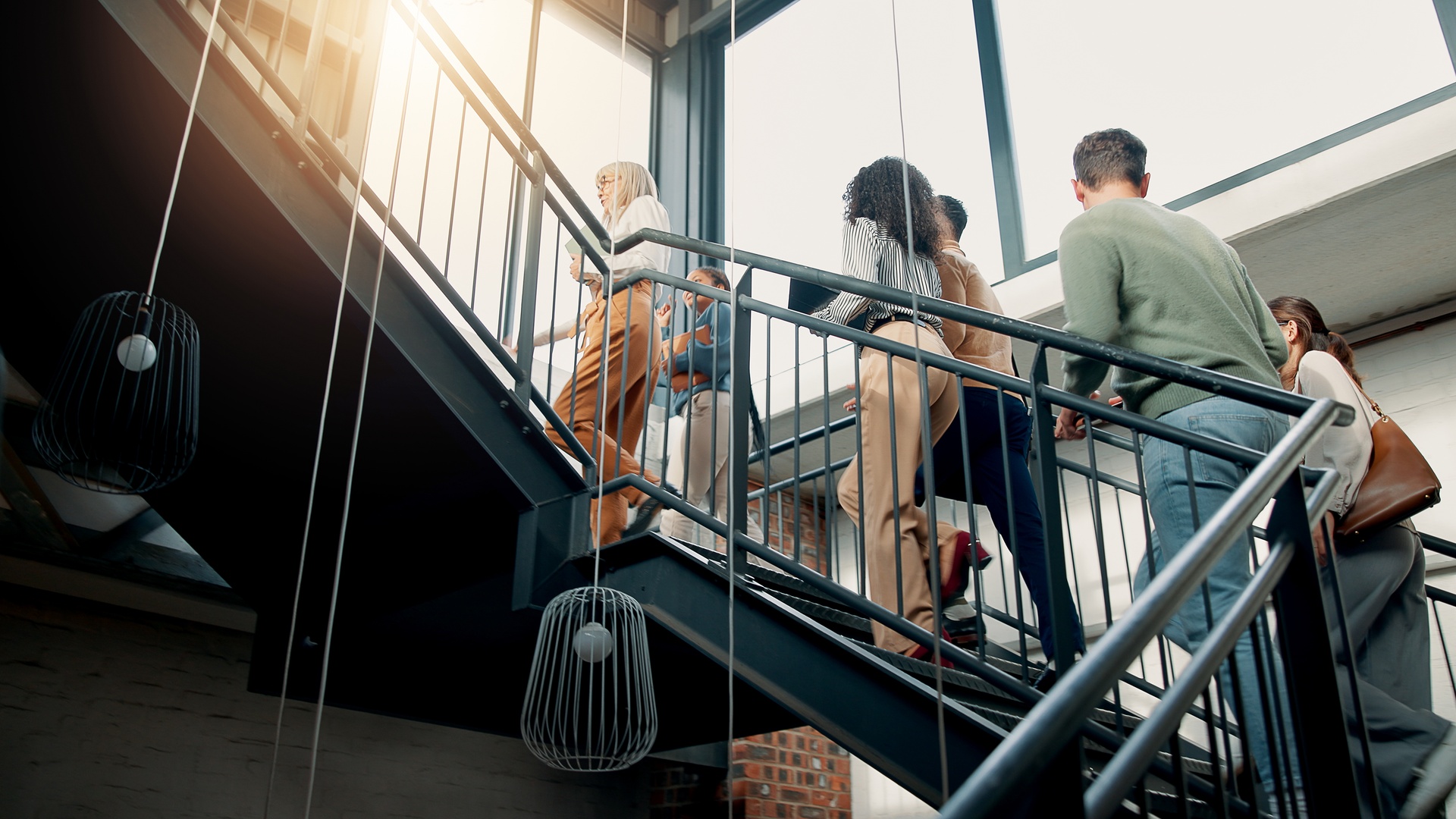 Male and female business professionals walk up a two-quarter turn staircase. The railings are black and made of metal.