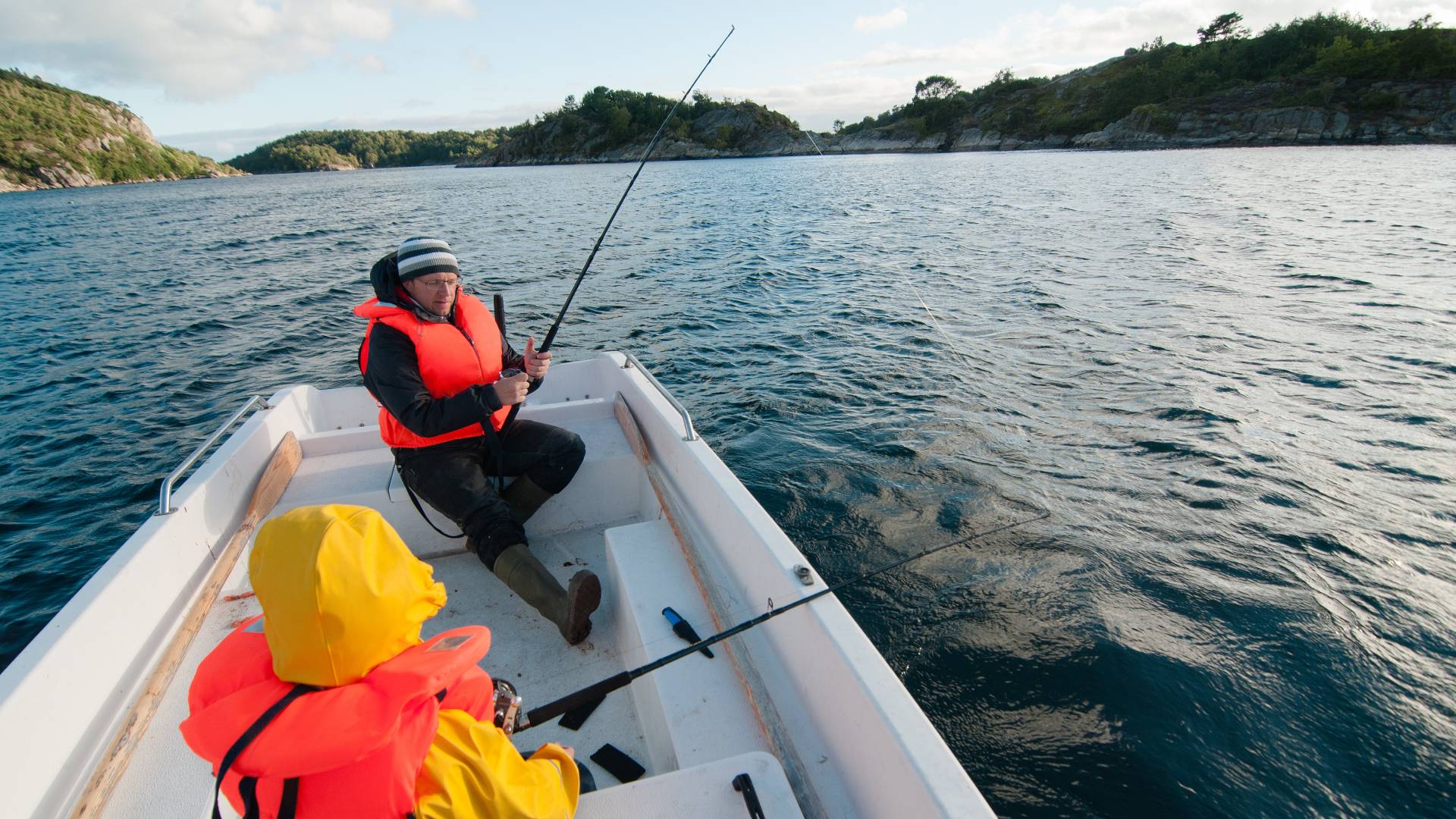  Two people sit across from each other on a small fishing boat in the middle of a lake with hills in the background.