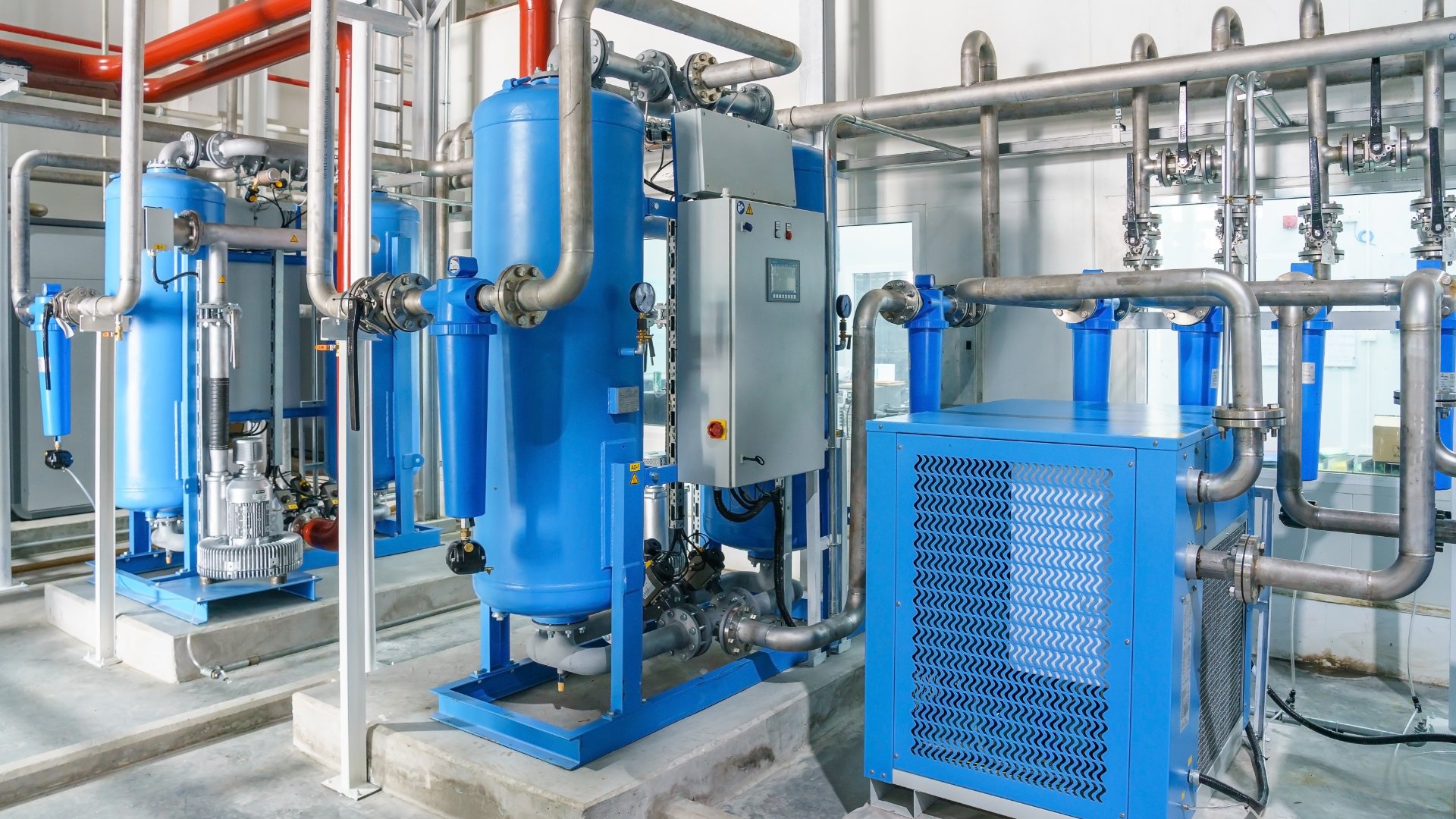A blue refrigerated air dryer for compressor air on a concrete floor in a bare room with white walls.