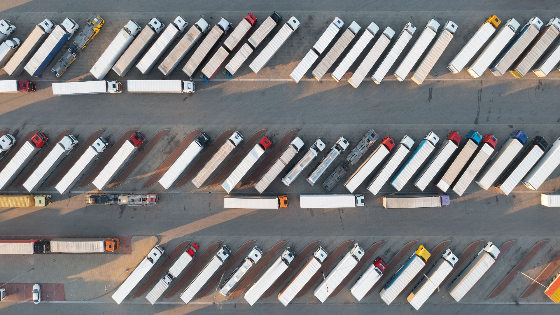 A bird’s eye view of a large parking lot filled with several semi-trucks all parked in diagonal parking spots.