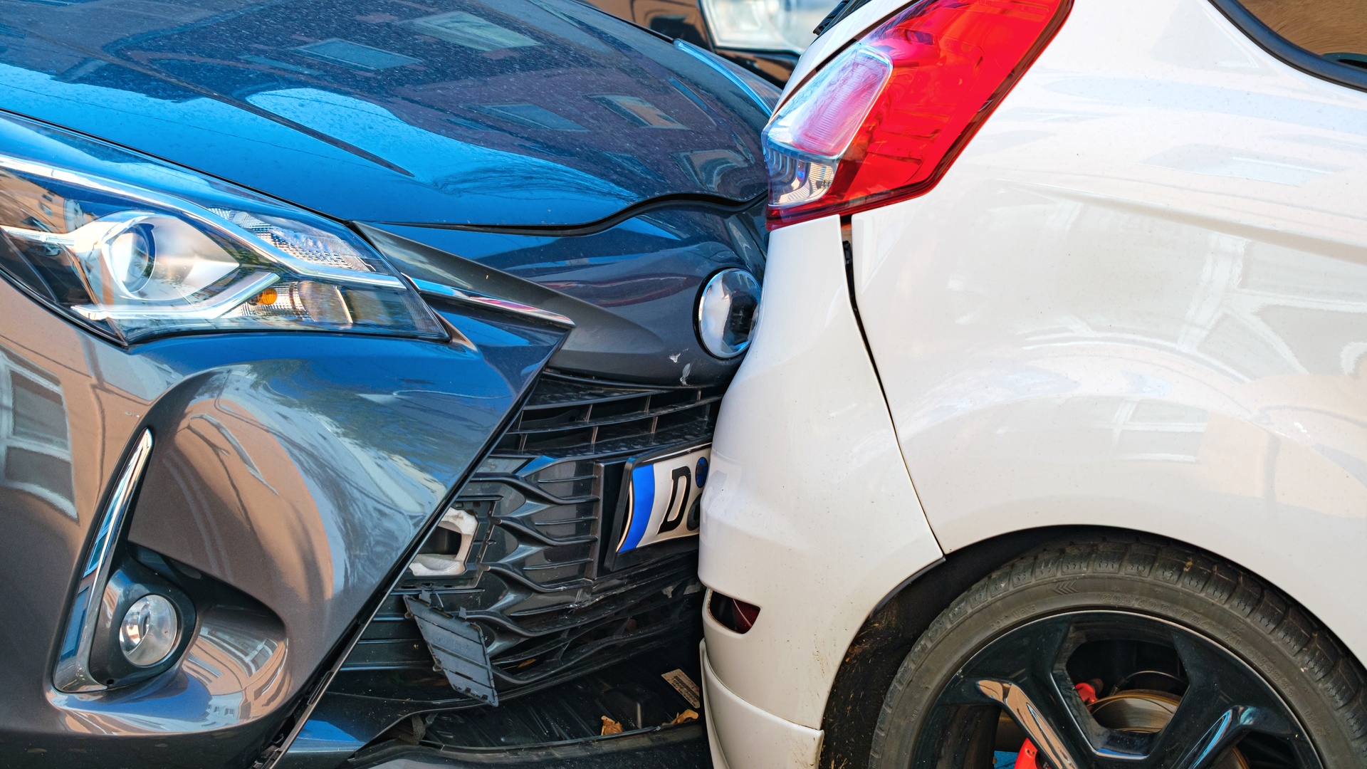 Two cars involved in a crash with their rear and front bumpers touching each other. The bumpers have minor damage.