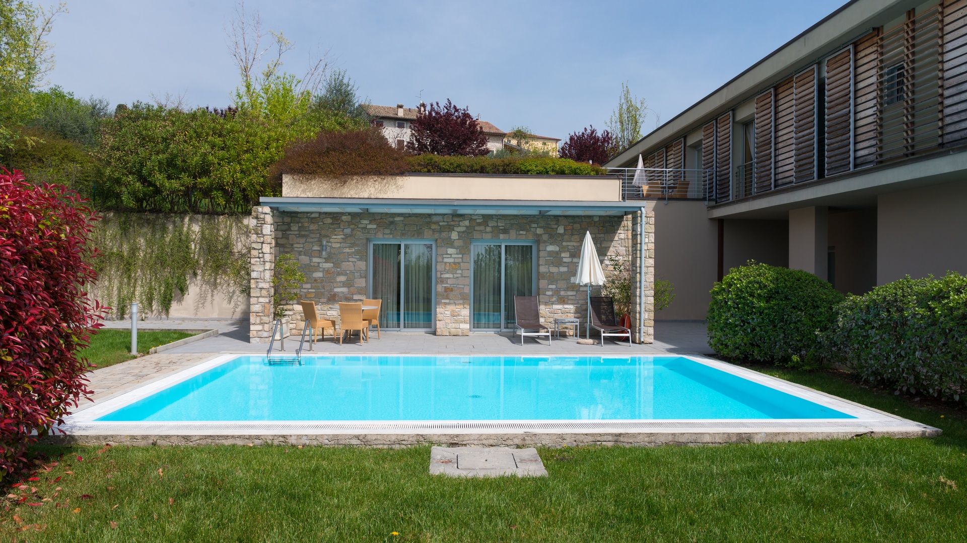 The backyard of a house with a swimming pool and a covered patio containing several seating options.