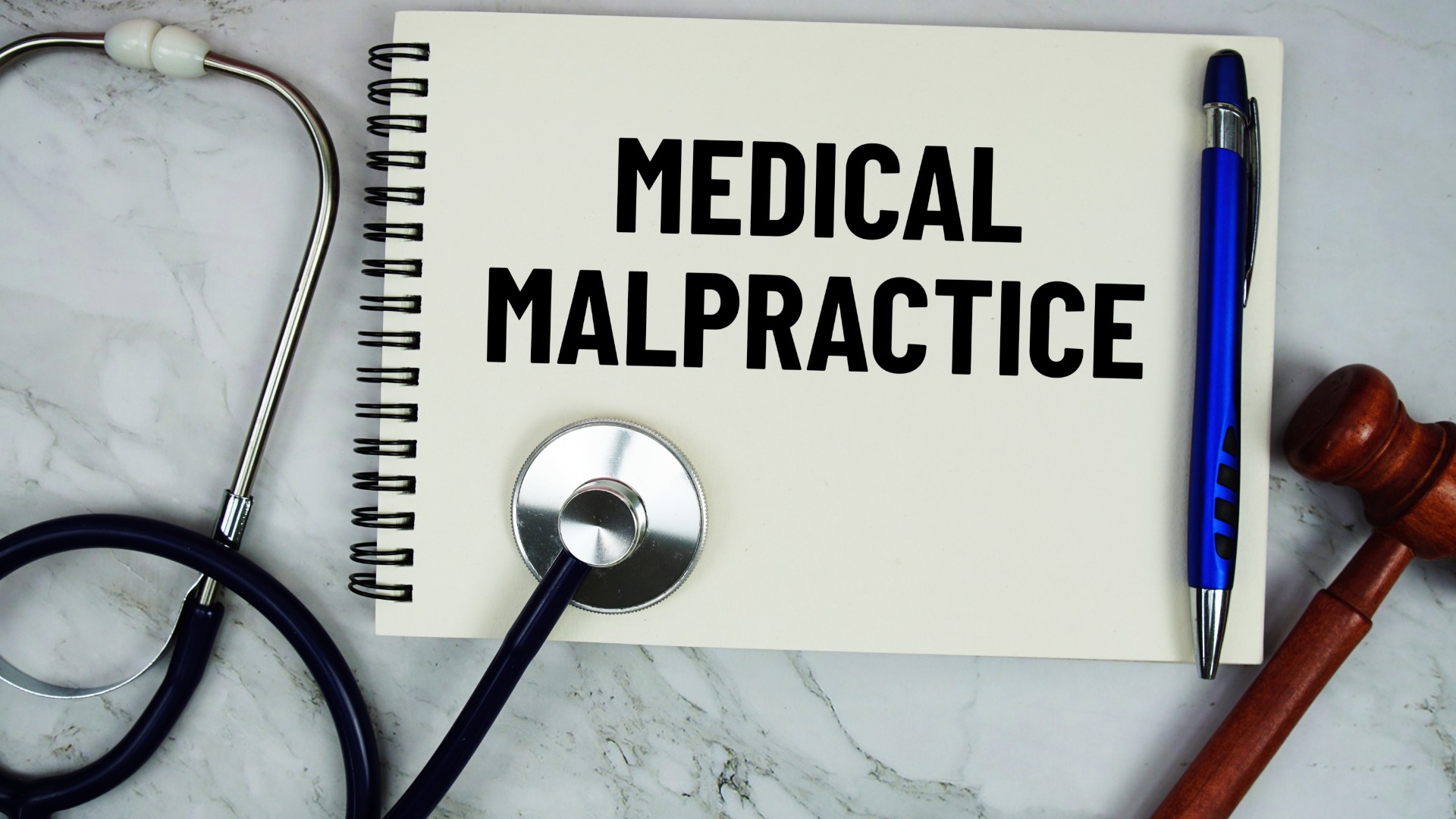 An aerial view of a notebook displaying the words “medical malpractice” on the cover next to a stethoscope and a gavel.