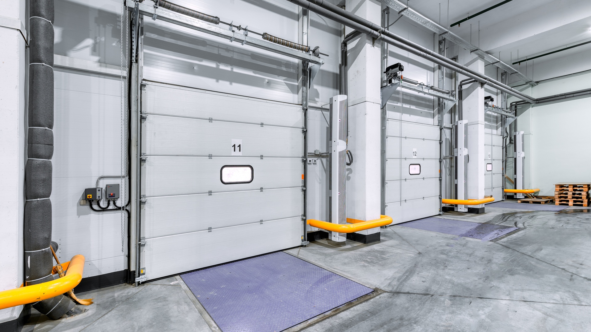 The loading gates of a large industrial warehouse. There are three large roll-up doors to load items into the building.