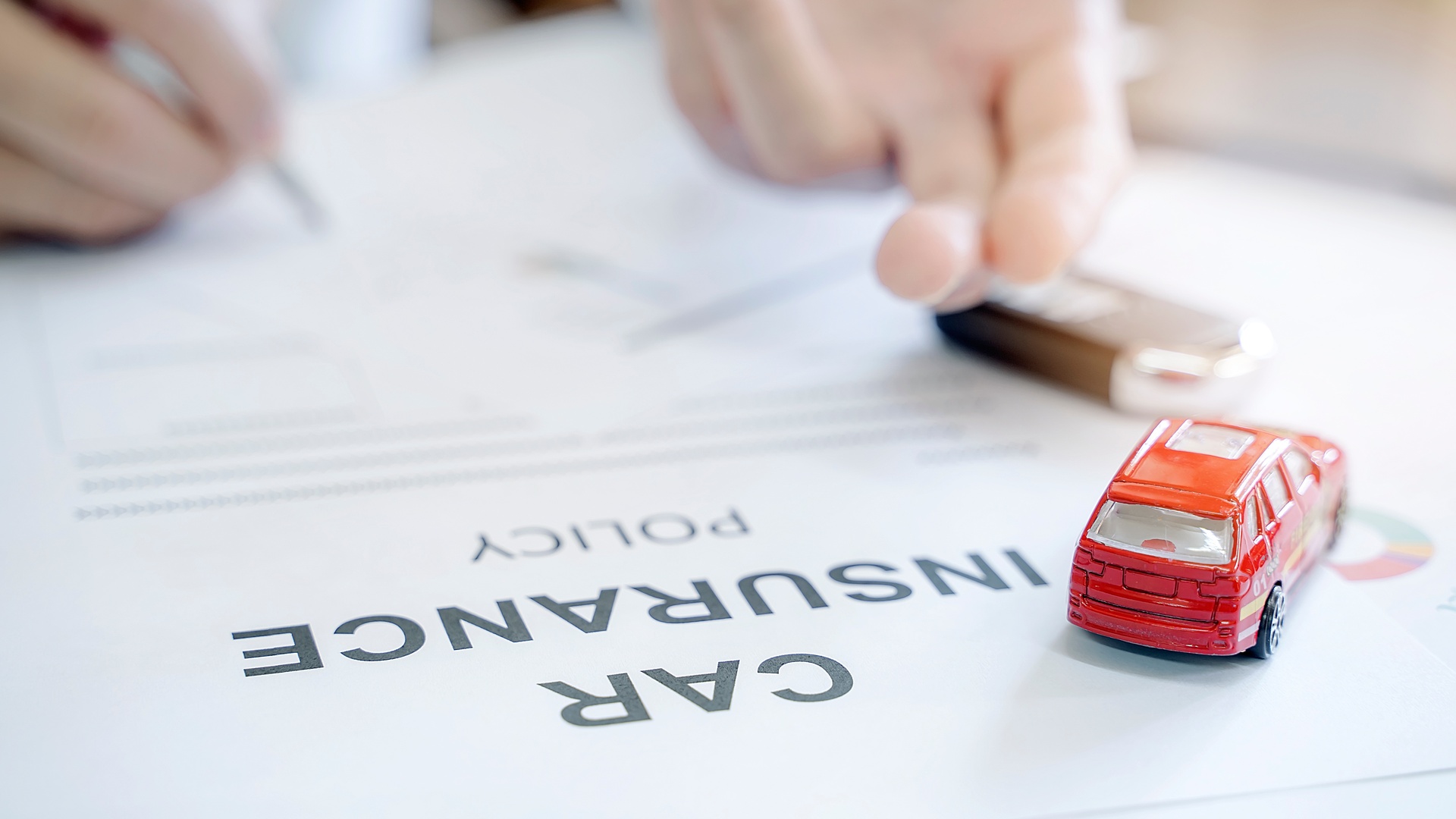 A white document titled "Car Insurance Policy," lays on a table near a small, red-colored toy car and a set of keys.