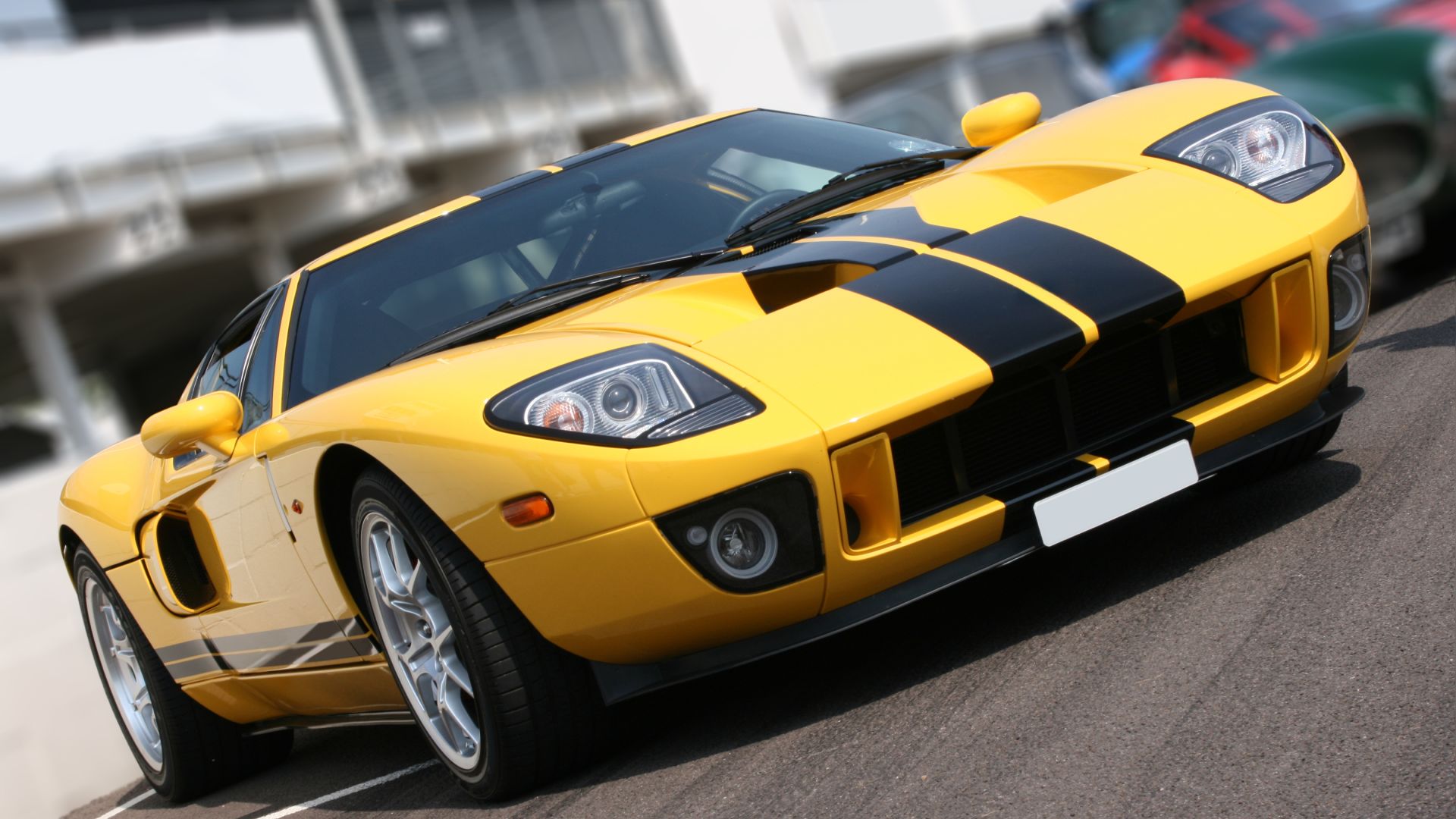 A yellow sports car is parked outside on a sunny day. There are black racing stripes on the top and side of the vehicle.