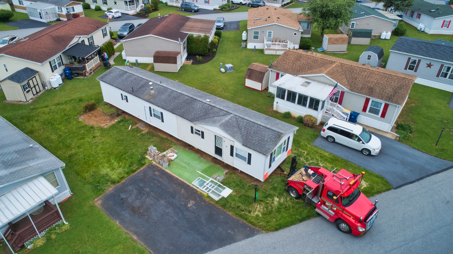 An aerial view of a long manufactured mobile home on a lot with a red truck positioned at the end in a residential park.