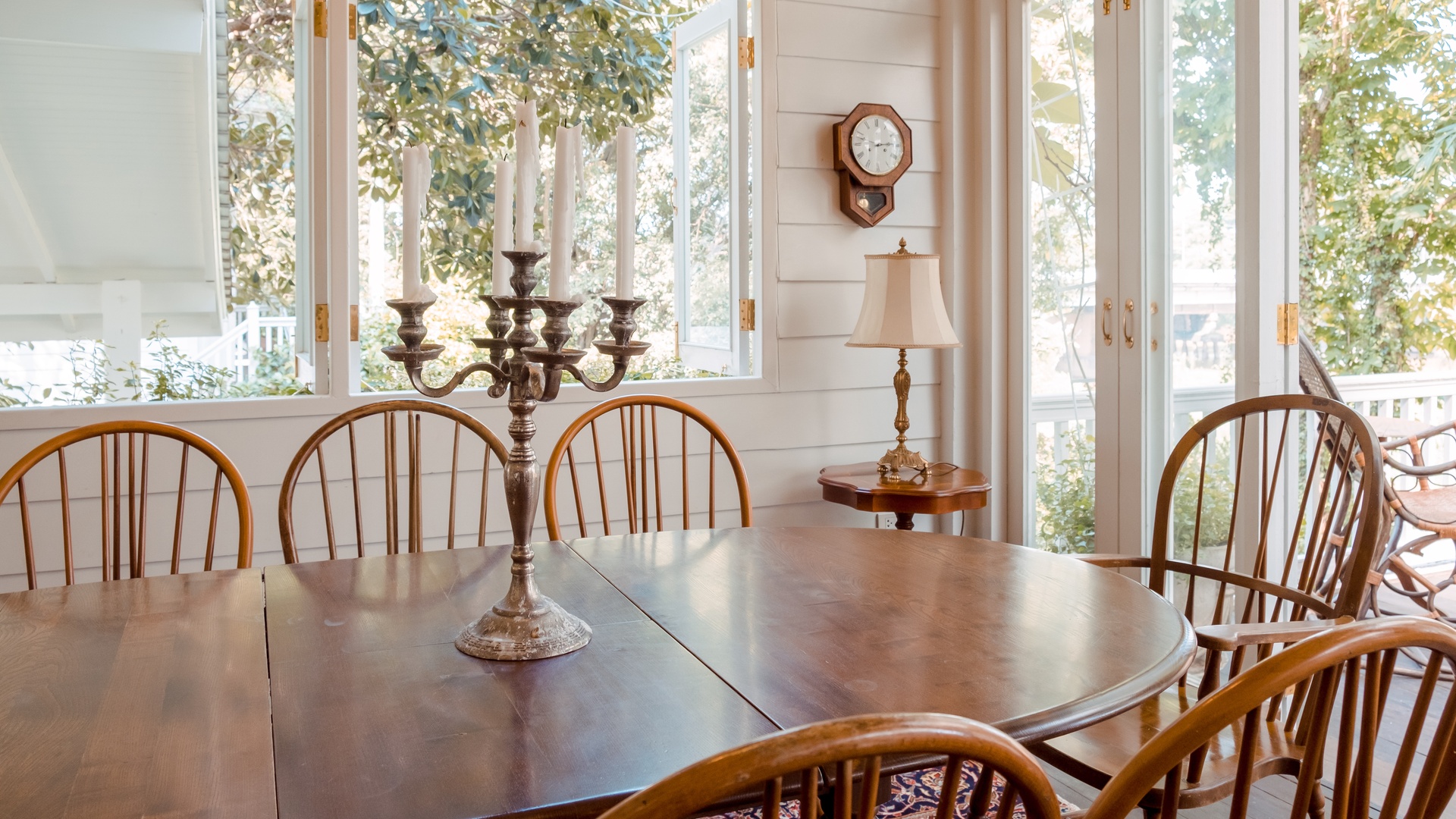 A classic dining room with vintage wooden chairs and a table, featuring an antique candle holder and a wall clock.