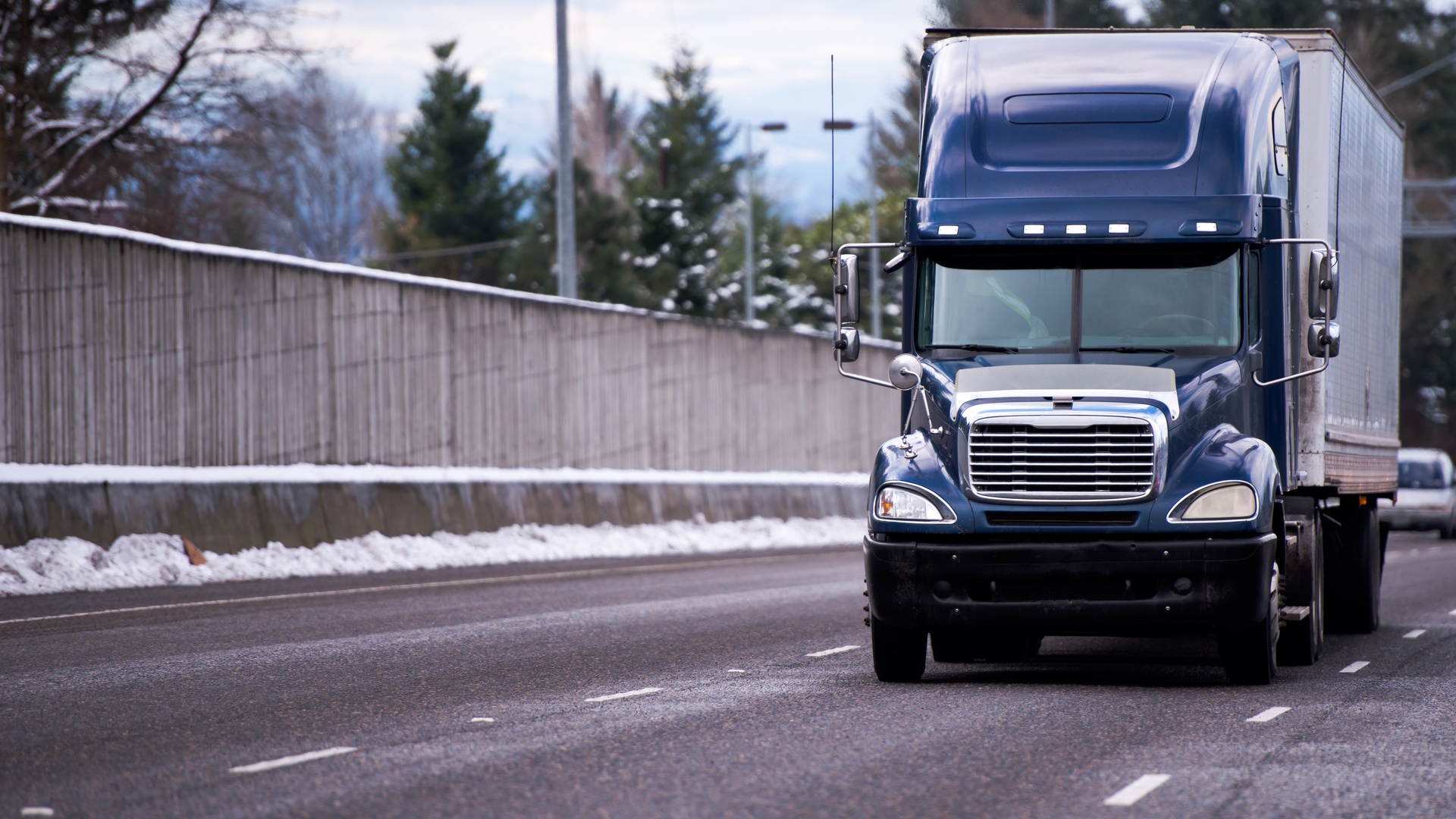 A single fleet truck with a blue cabin, driving through an empty street with light snow on the roadside.
