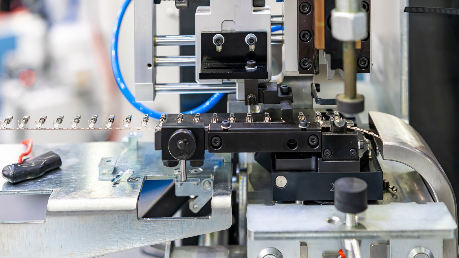  A side view of an automatic electrical terminal crimping machine with a long line of wire crimps in a work shop.