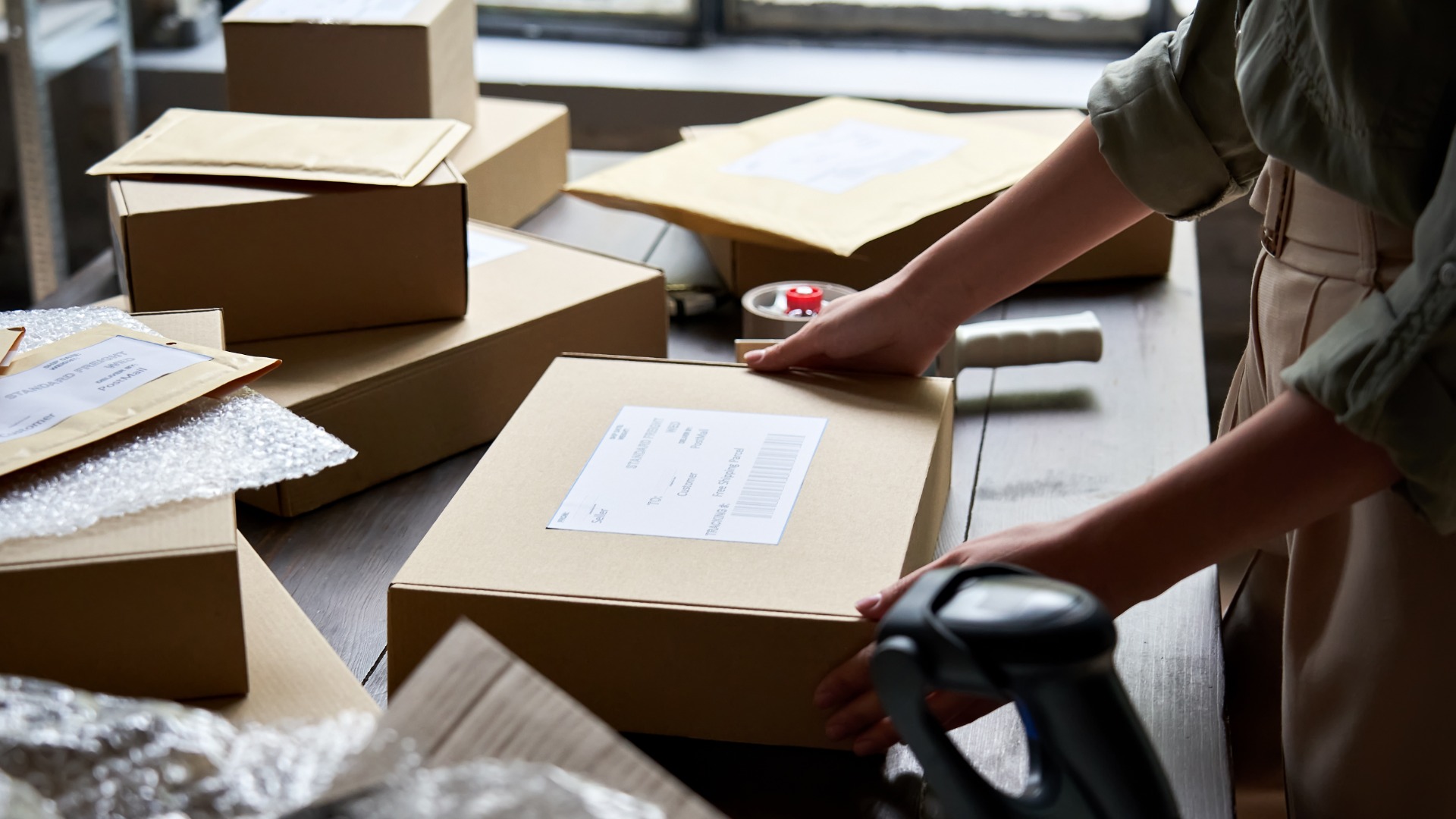 A person with rolled-up sleeves is placing their hands on a rectangular cardboard box that is sitting on a table.