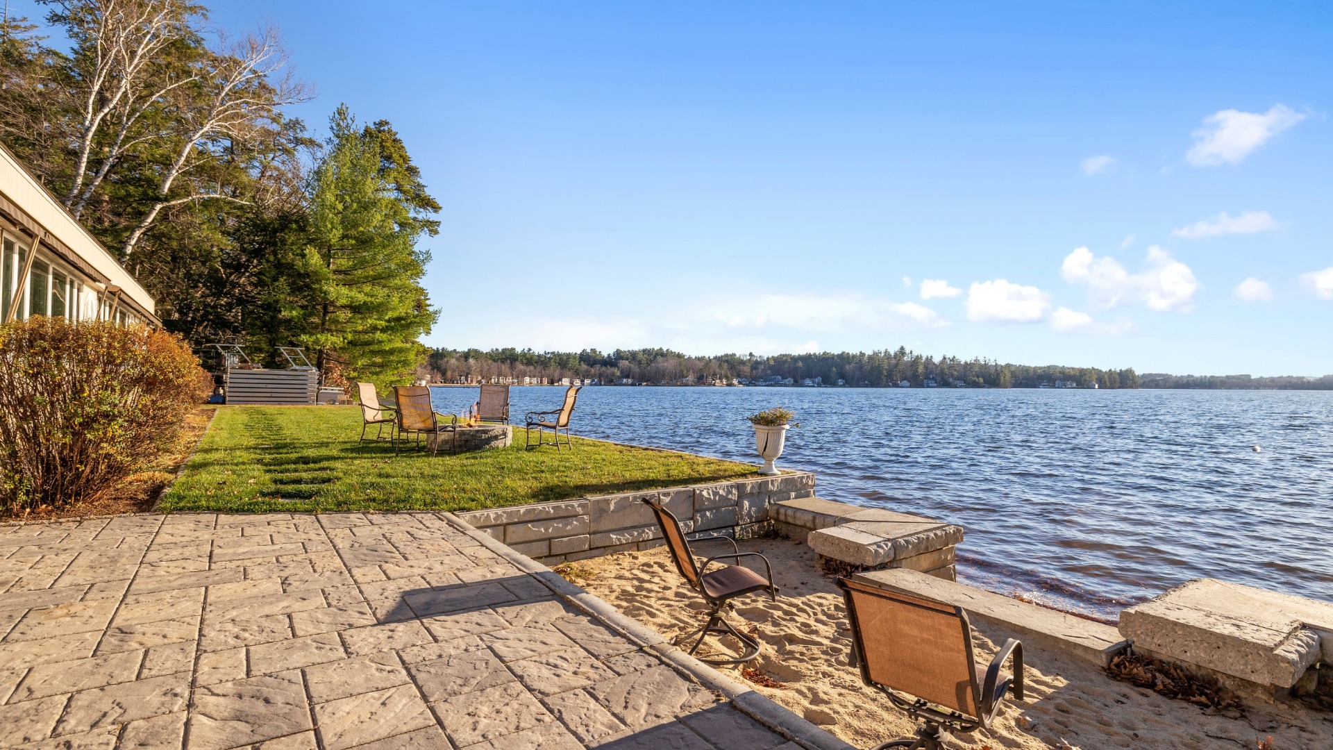 The backyard of a house that sits on a lakefront. There is a patio space that looks out on the clear lake.