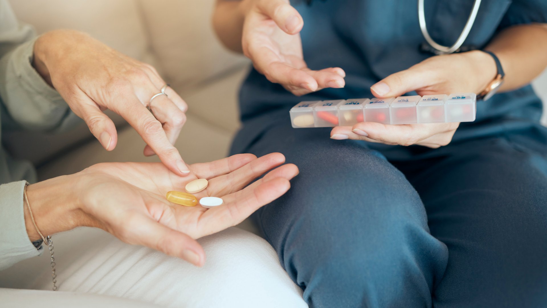 A close-up of a pair of hands holding three pills and another pair of hands holding a clear organizer full of pills.