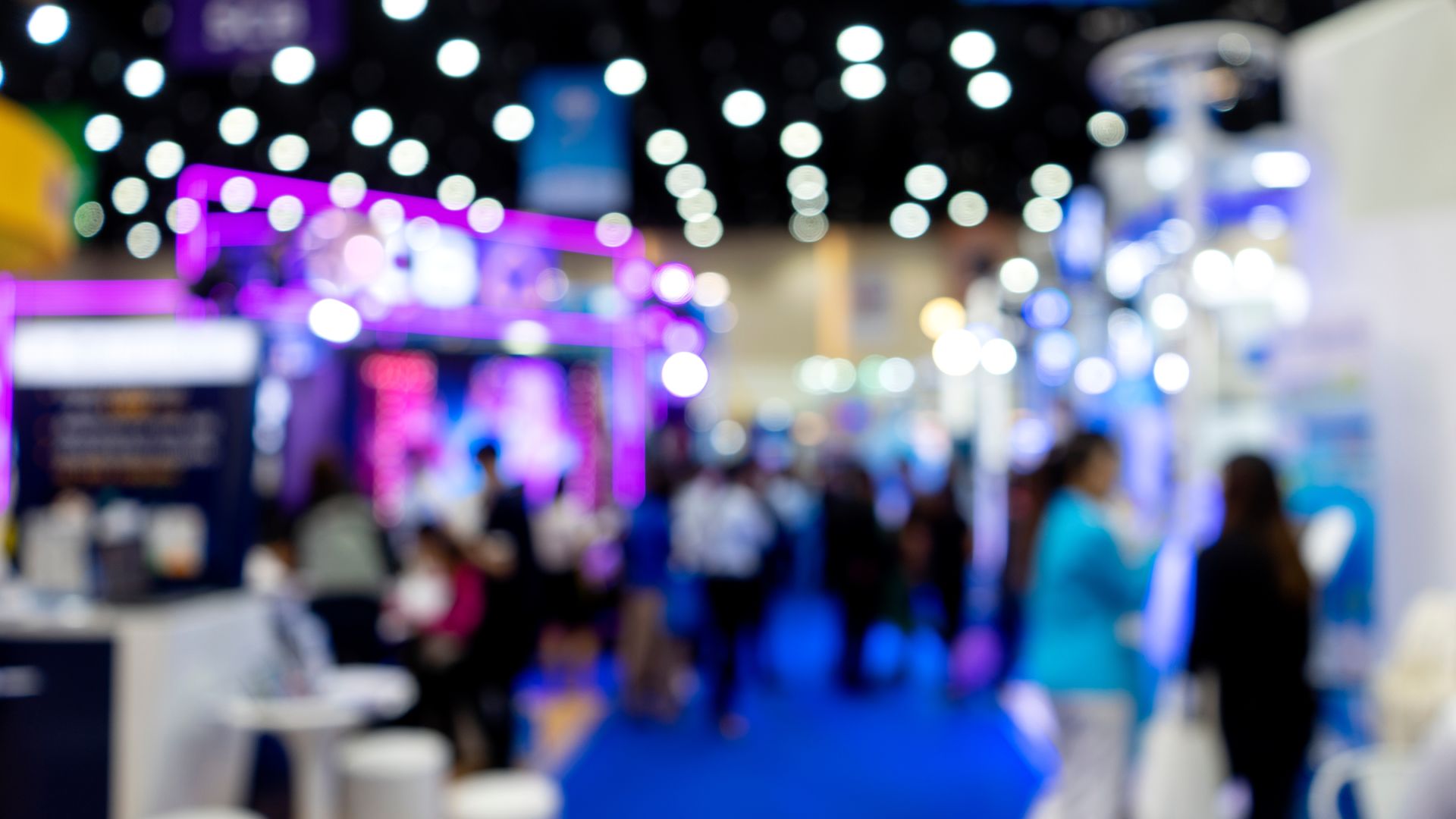 a blurred image of a trade show convention with twinkling lights and a large crowd of people walking around.