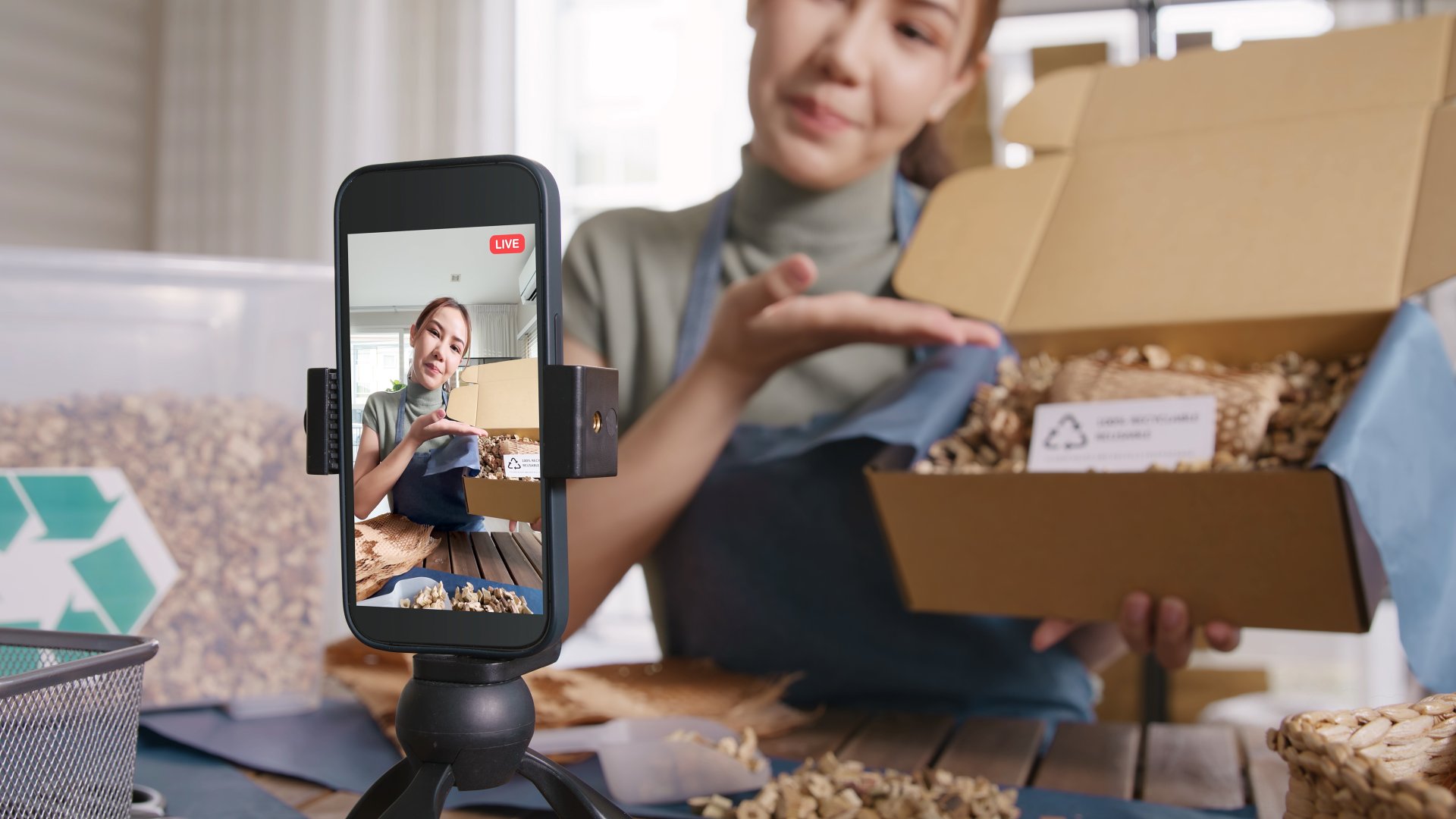 A female shopkeeper films herself showing off the contents of a box of product, likely for social media.