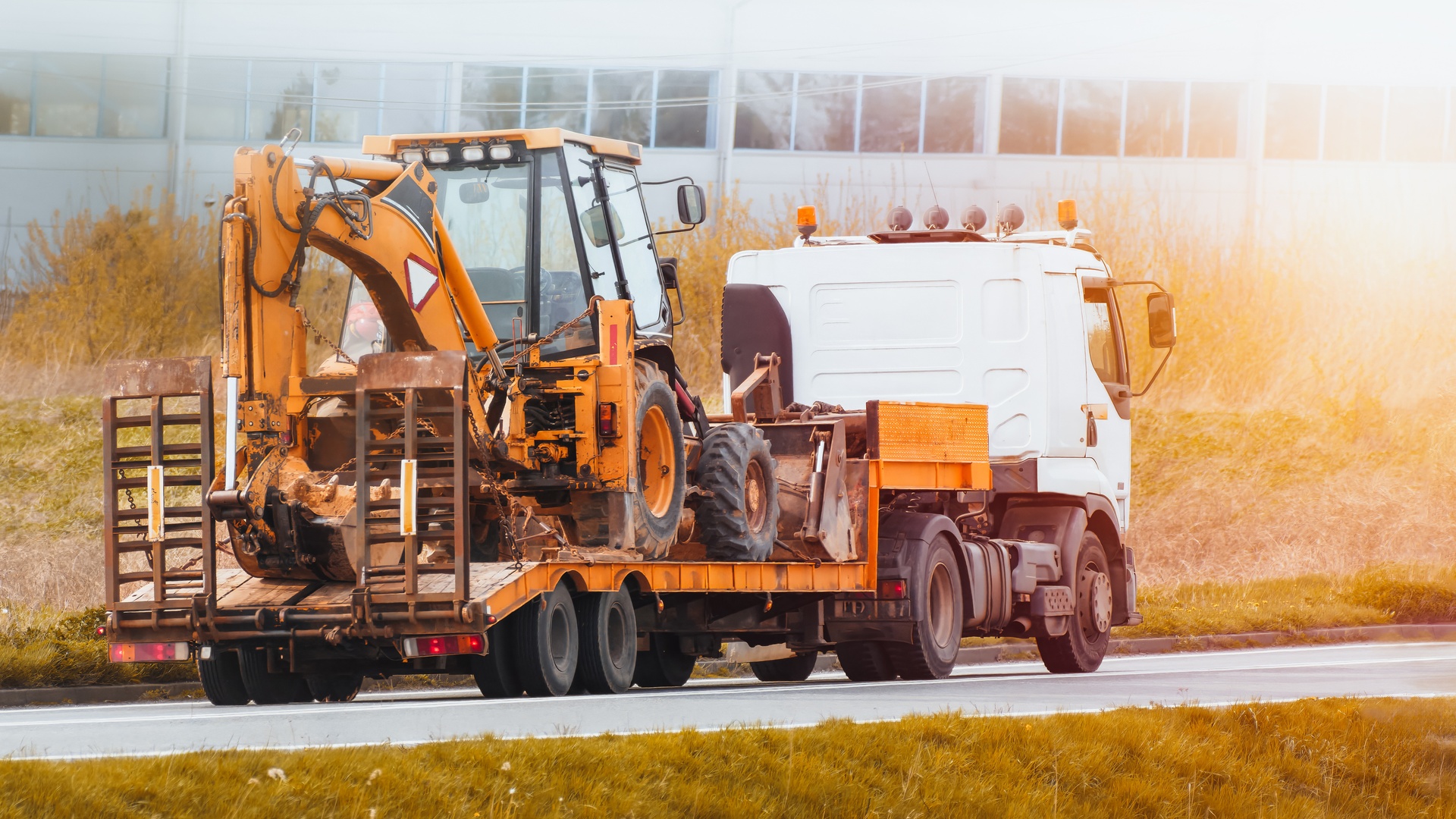 A flatbed truck driving on the road during the daytime. The truck is transporting an excavator tractor.