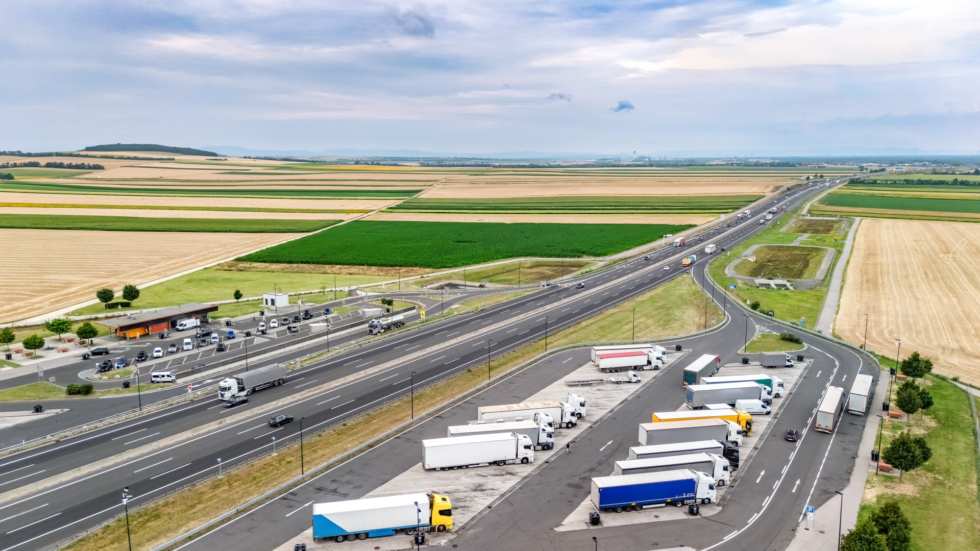 A truck rest stop on the side of a highway. The highway is cutting through the middle of farmland country.