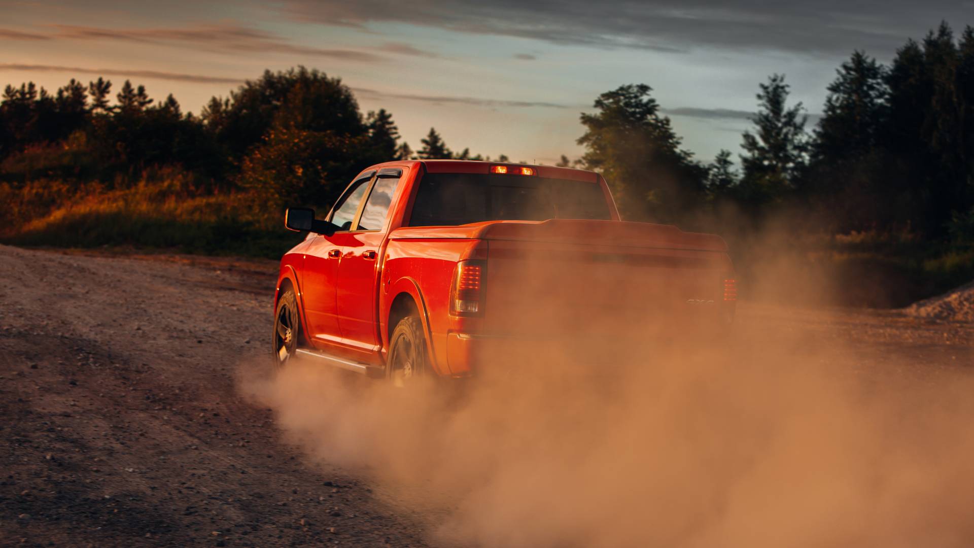 A large red pickup truck from behind, speeding away down a rural road and kicking up a big cloud of dust.