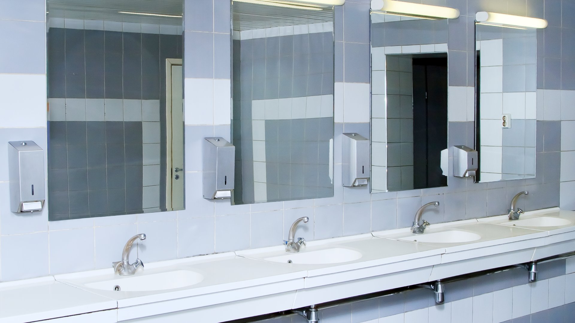 A public bathroom sink area with four sinks. Above each sink are four separated, tall, rectangular mirrors.