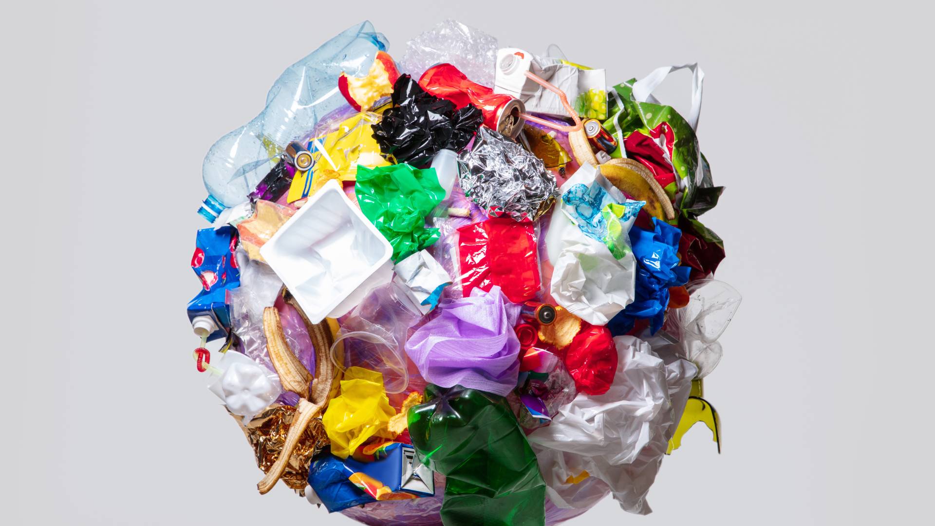 A giant wad of various metal, plastic, glass, organic, and other waste and trash floats in an empty gray field.