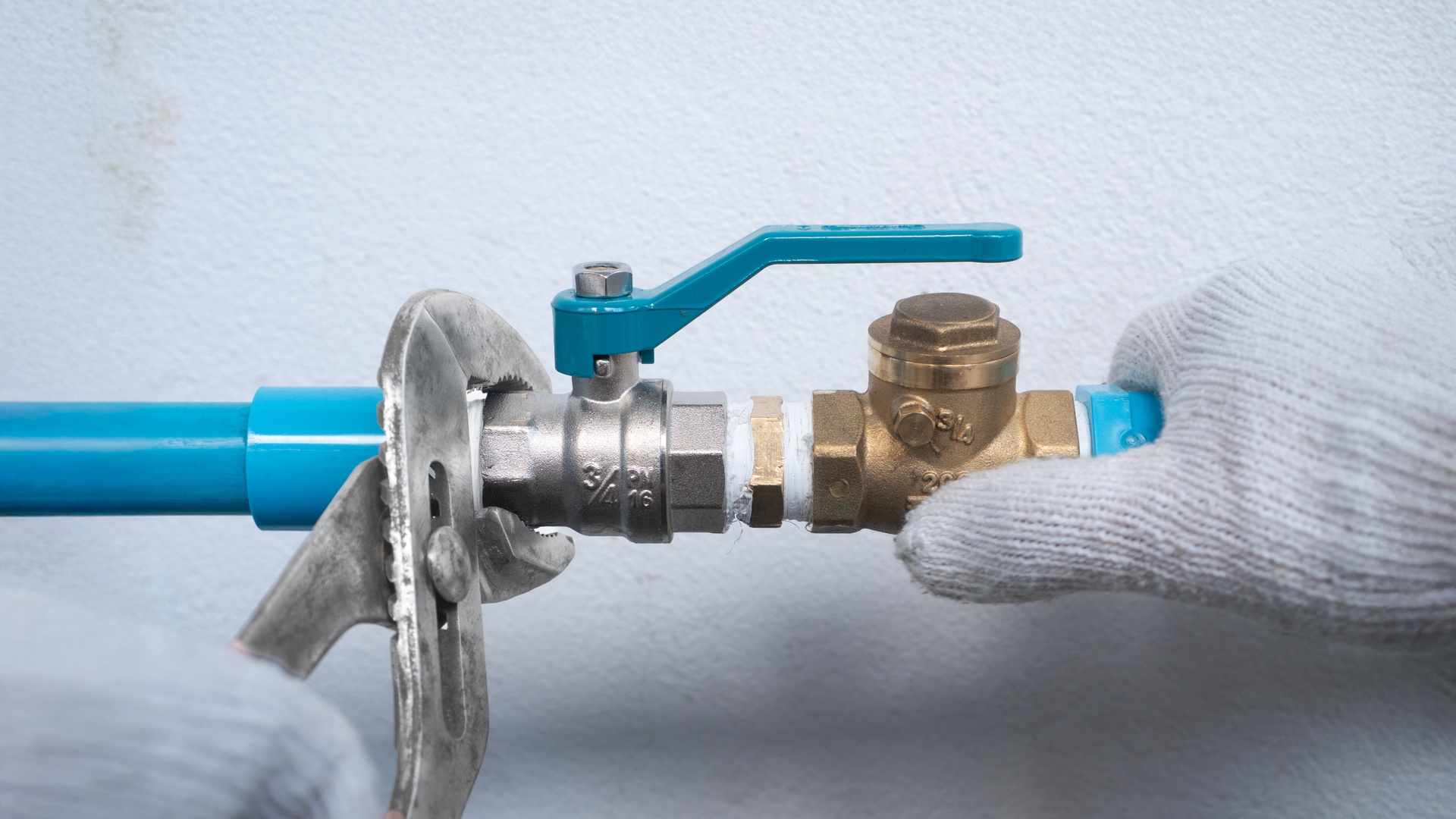 A blue pipe connected to a water pump handle and a gloved hand gripping one end of the pipe with a wrench at the other end.