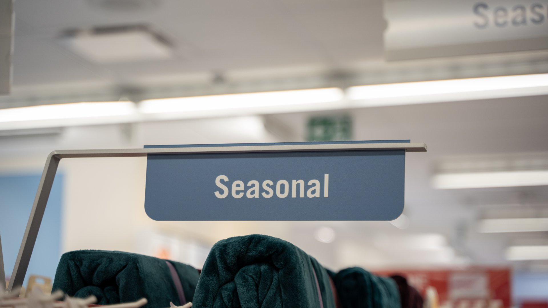 A close-up of a sign inside a store that reads "Seasonal." Underneath the sign are green blankets carefully folded.